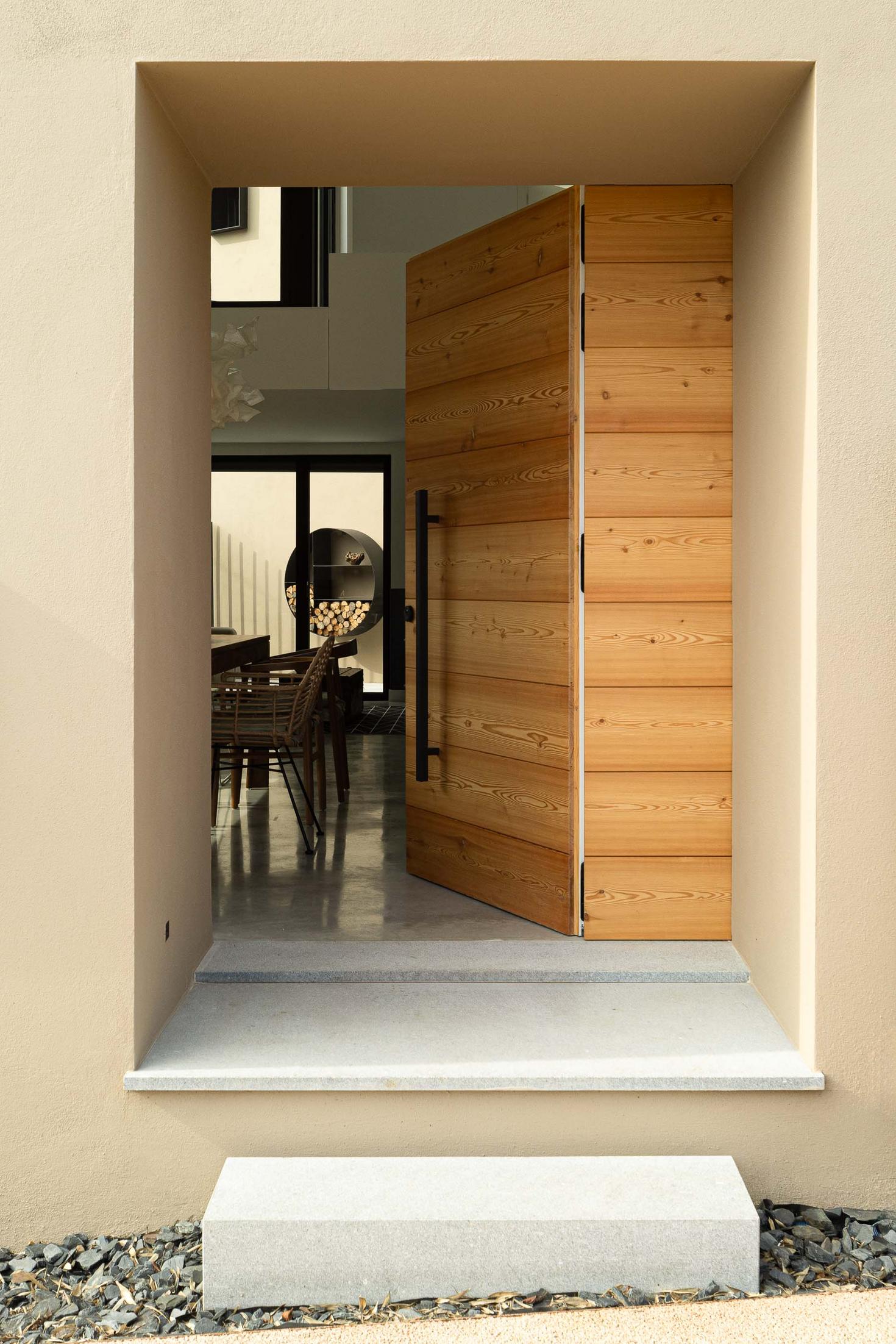 Entrada: Porta de madeira maciça aberta para o interior da casa, com pavimento cinzento. — CASINHA DA MELROEIRA arquitetura Filipe Saraiva Arquitectos em Ourém