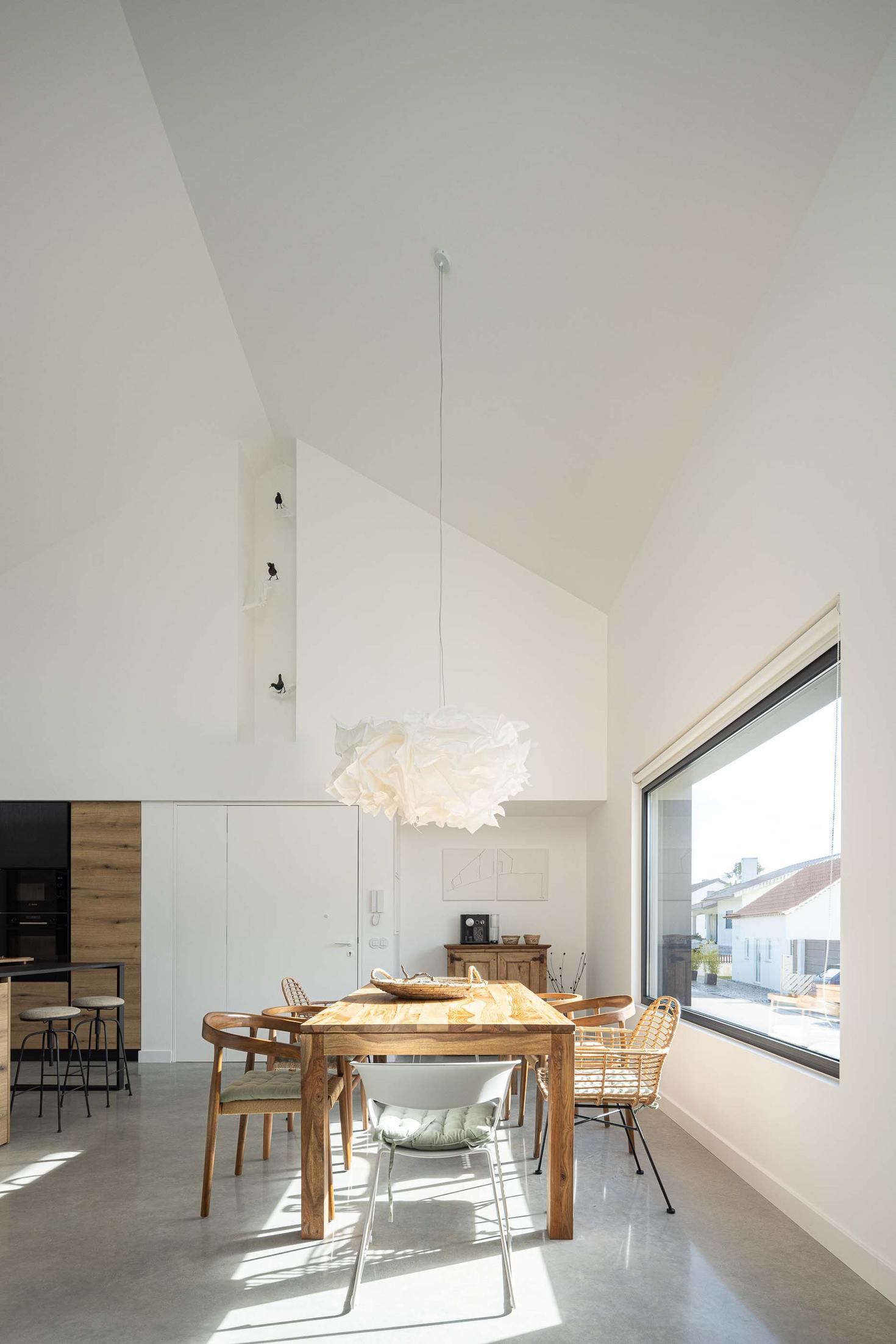 Sala de jantar: Vista da sala de jantar com mesa de madeira, cadeiras e candeeiro moderno. — CASINHA DA MELROEIRA arquitetura Filipe Saraiva Arquitectos em Ourém