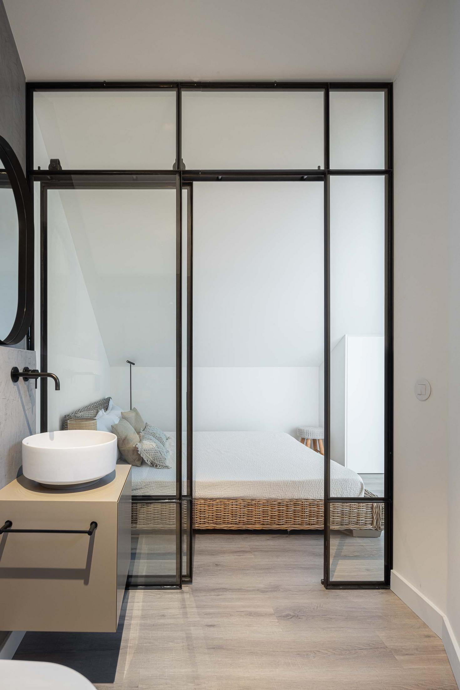 Casa de banho: Lavatório branco, espelho redondo e divisória de vidro preto para o quarto. — CASINHA DA MELROEIRA arquitetura Filipe Saraiva Arquitectos em Ourém