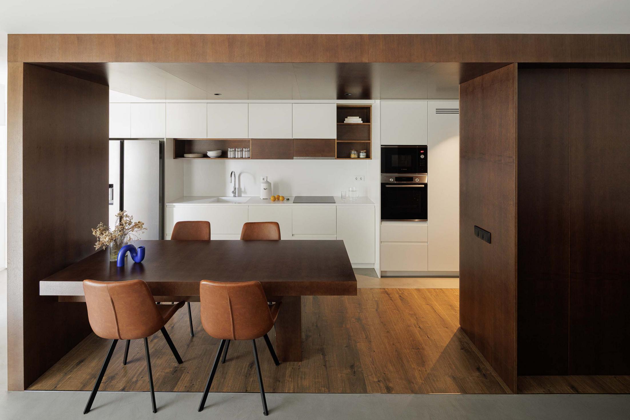 Cozinha/Sala de jantar: Mesa de madeira escura com cadeiras em pele castanha, armários brancos e apontamentos em madeira escura. Pavimento em madeira. — APARTAMENTO FP arquitetura ArquitectosRT em Braga