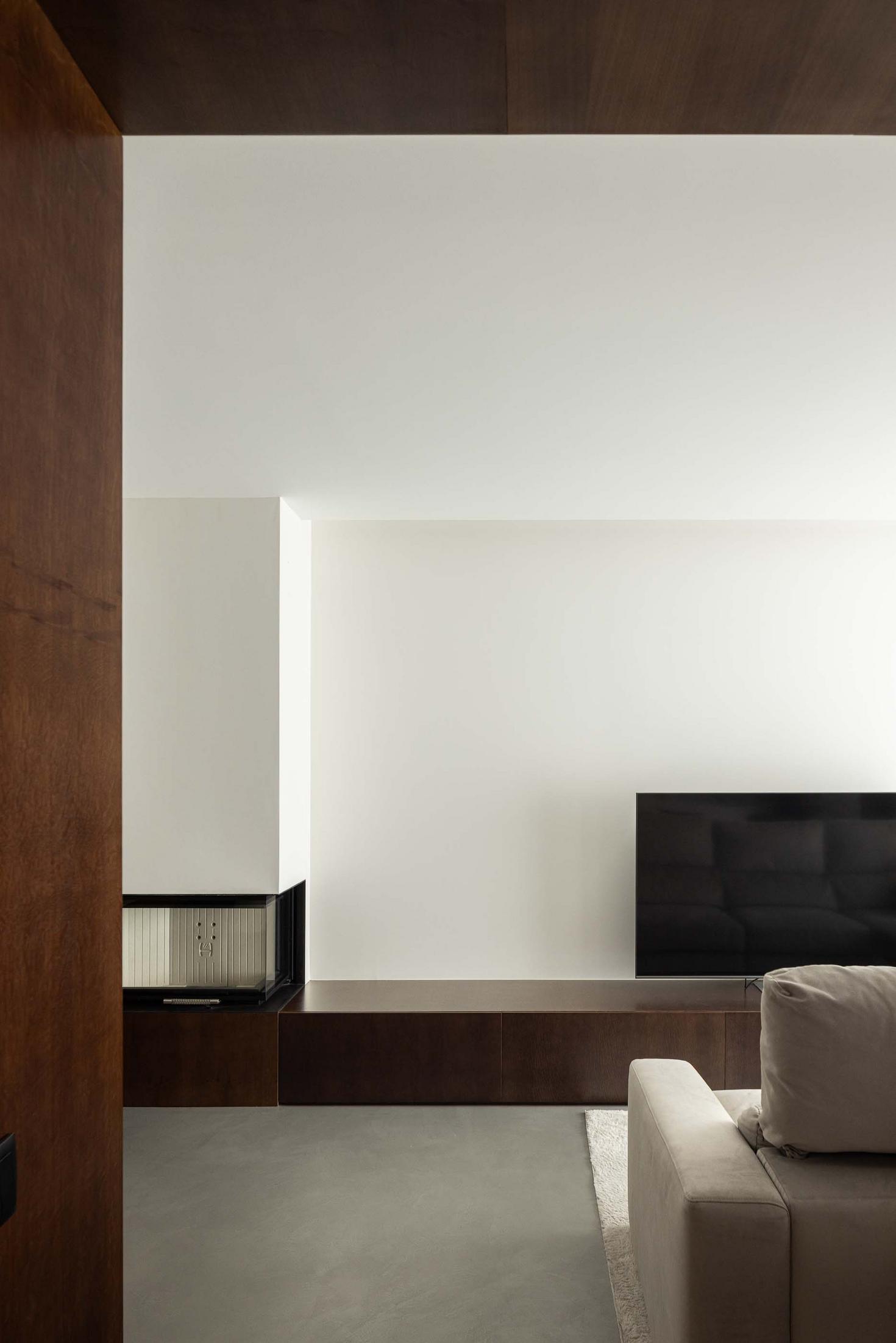 Sala de estar: Lareira moderna. Móvel de televisão em madeira escura. Sofá branco. Pavimento em cimento. — APARTAMENTO FP arquitetura ArquitectosRT em Braga