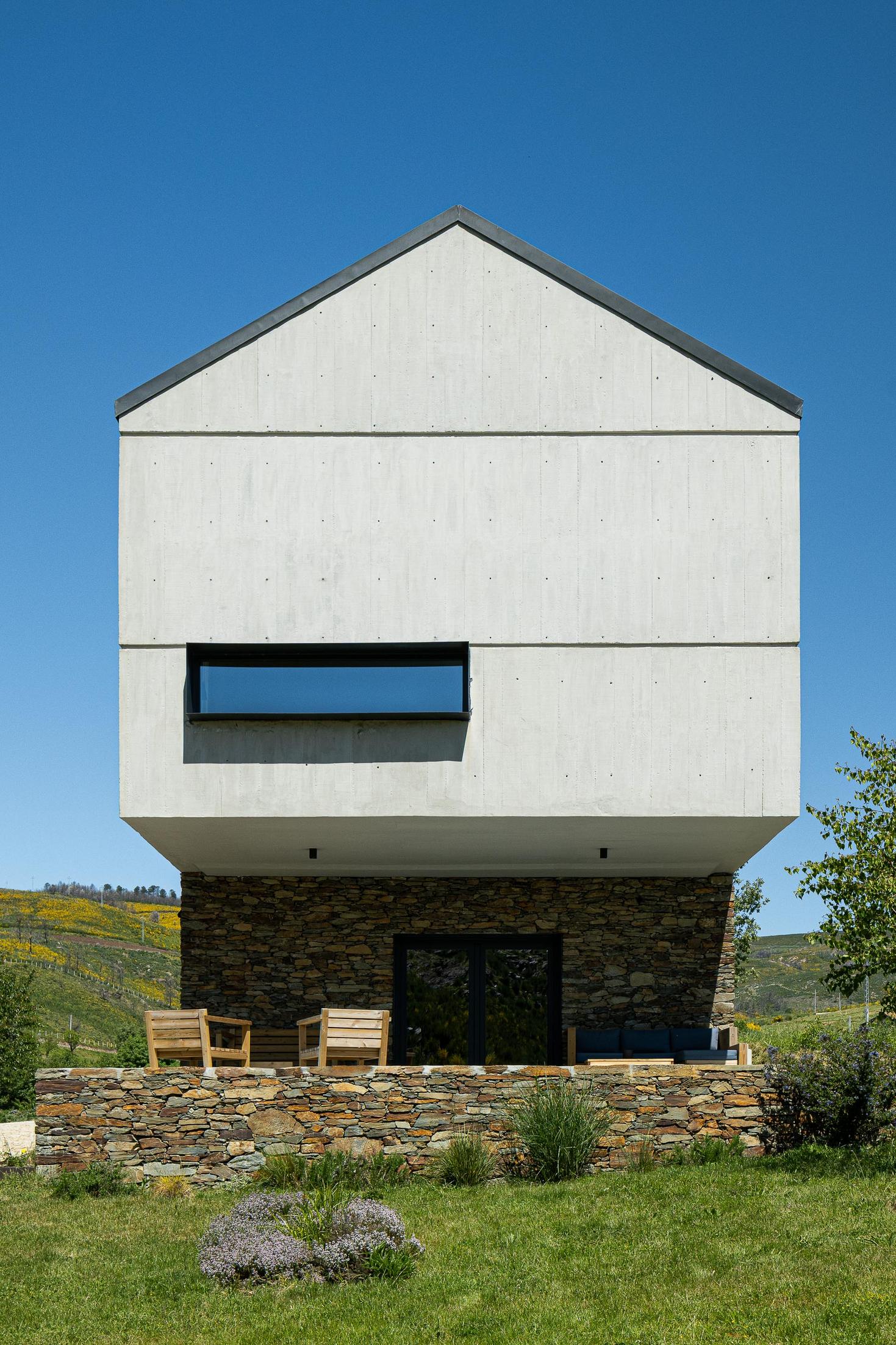 Exterior: Fachada principal da casa com base em pedra e volume superior em betão aparente. — TerraSense Mountain Charm Retreat arquitetura DRK Atelier em Guarda