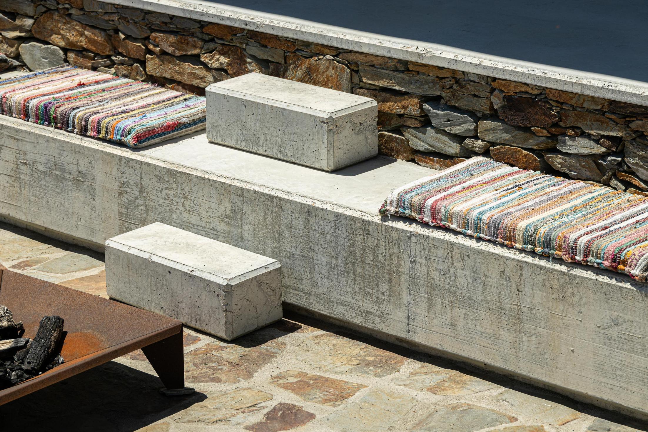 Exterior: Detalhe de sofás embutidos em betão com almofadas coloridas e lareira. — TerraSense Mountain Charm Retreat arquitetura DRK Atelier em Guarda