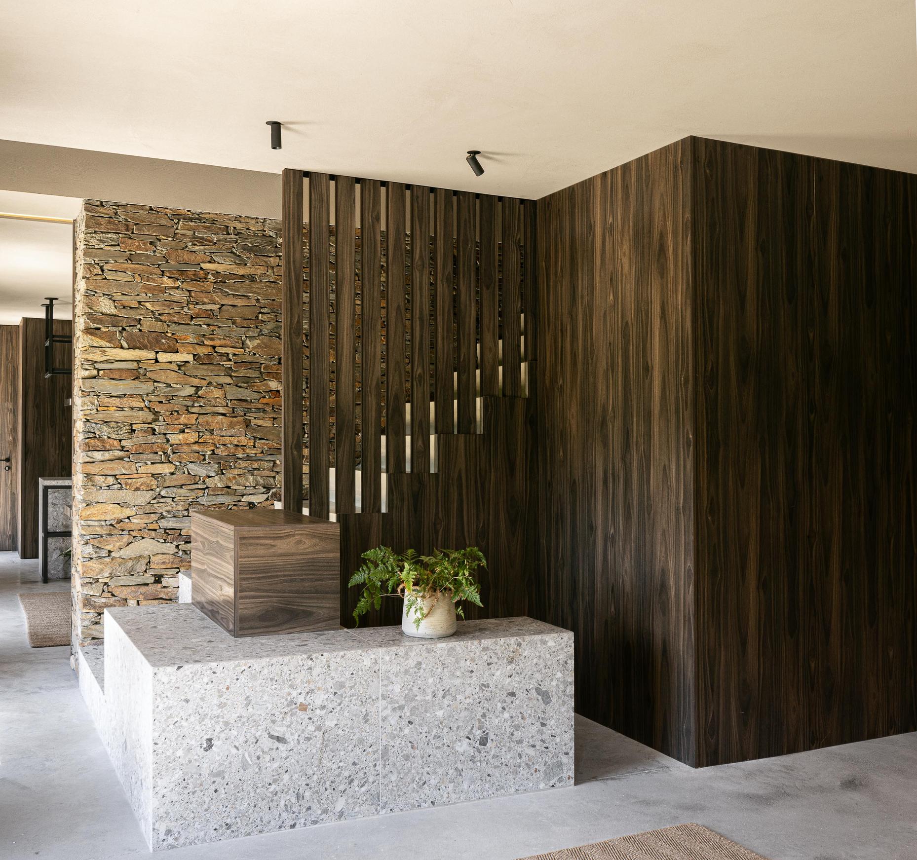 Hall de entrada: Balcão em granito com detalhes em madeira, parede em pedra e painéis em madeira. — TerraSense Mountain Charm Retreat arquitetura DRK Atelier em Guarda