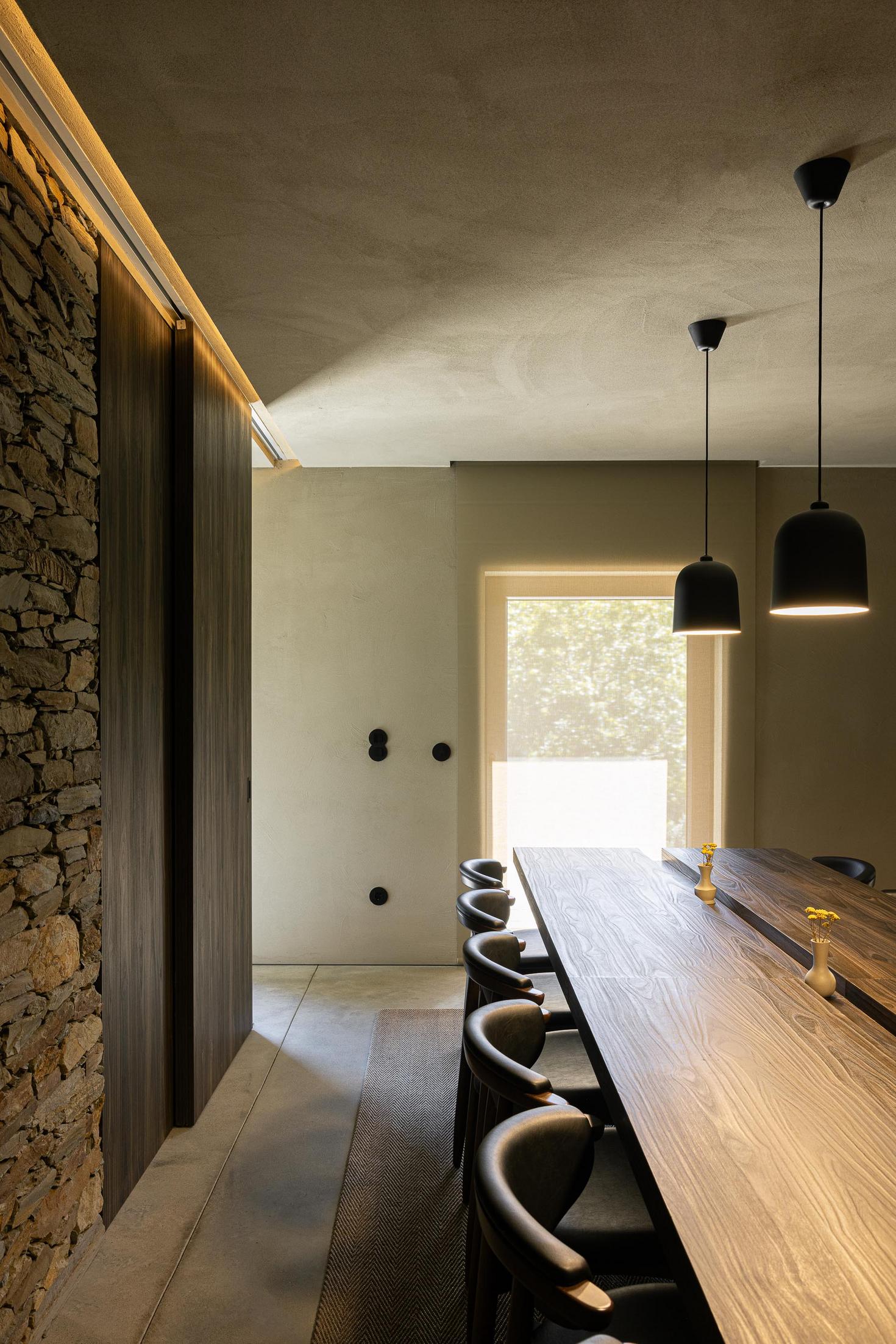 Sala de jantar: Mesa comprida em madeira com cadeiras pretas e candeeiros suspensos. — TerraSense Mountain Charm Retreat arquitetura DRK Atelier em Guarda