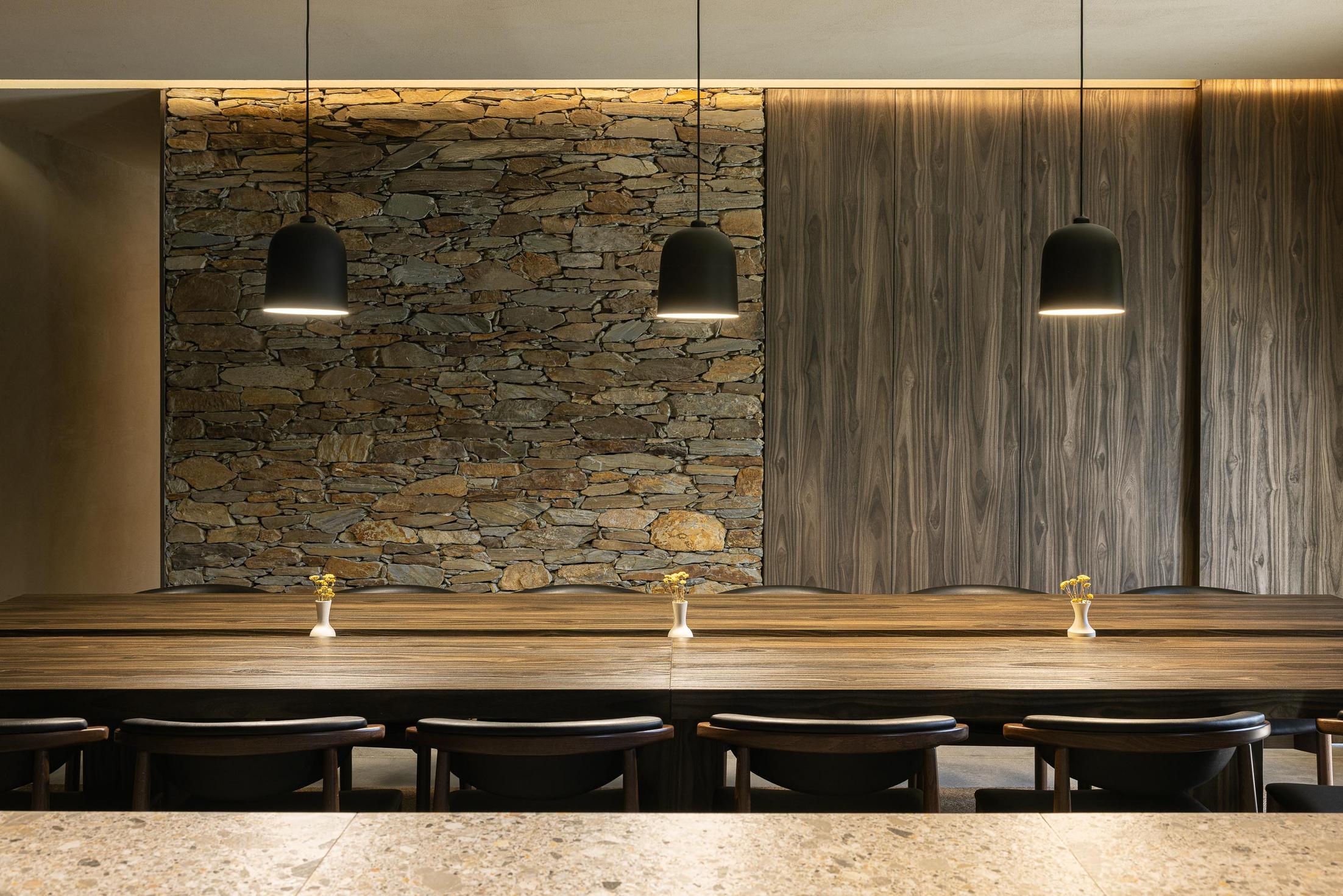 Sala de jantar: Detalhe da mesa em madeira com candeeiros pretos e parede em pedra. — TerraSense Mountain Charm Retreat arquitetura DRK Atelier em Guarda