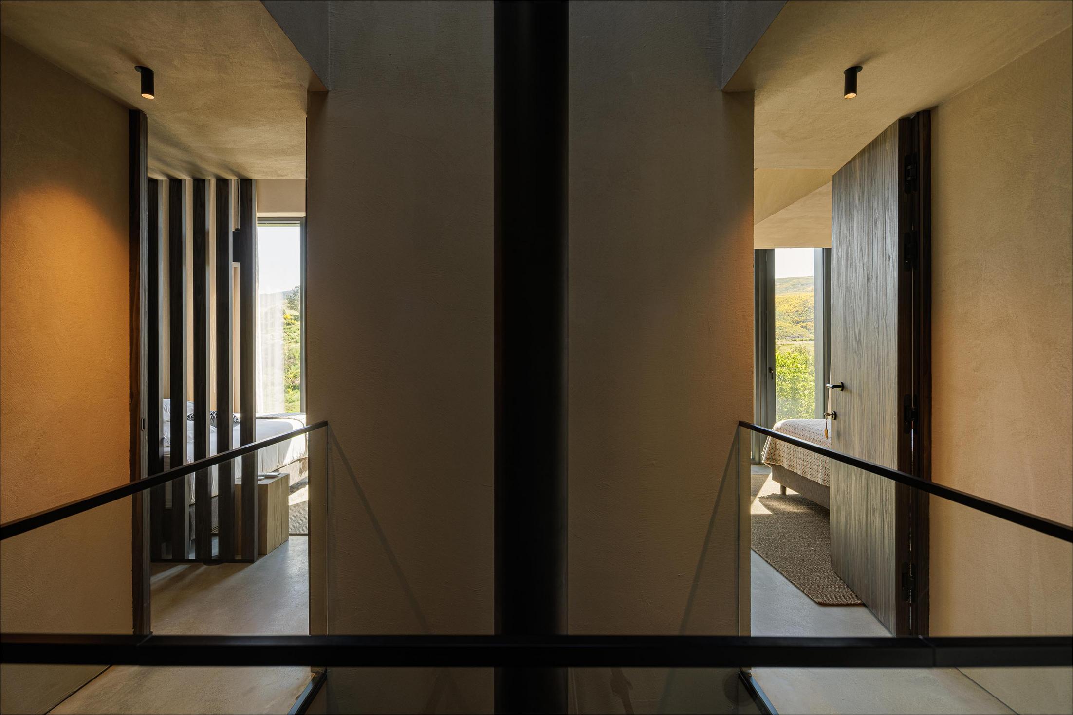 Corredor: Corredor no piso superior com vista para os quartos e guarda em vidro. — TerraSense Mountain Charm Retreat arquitetura DRK Atelier em Guarda