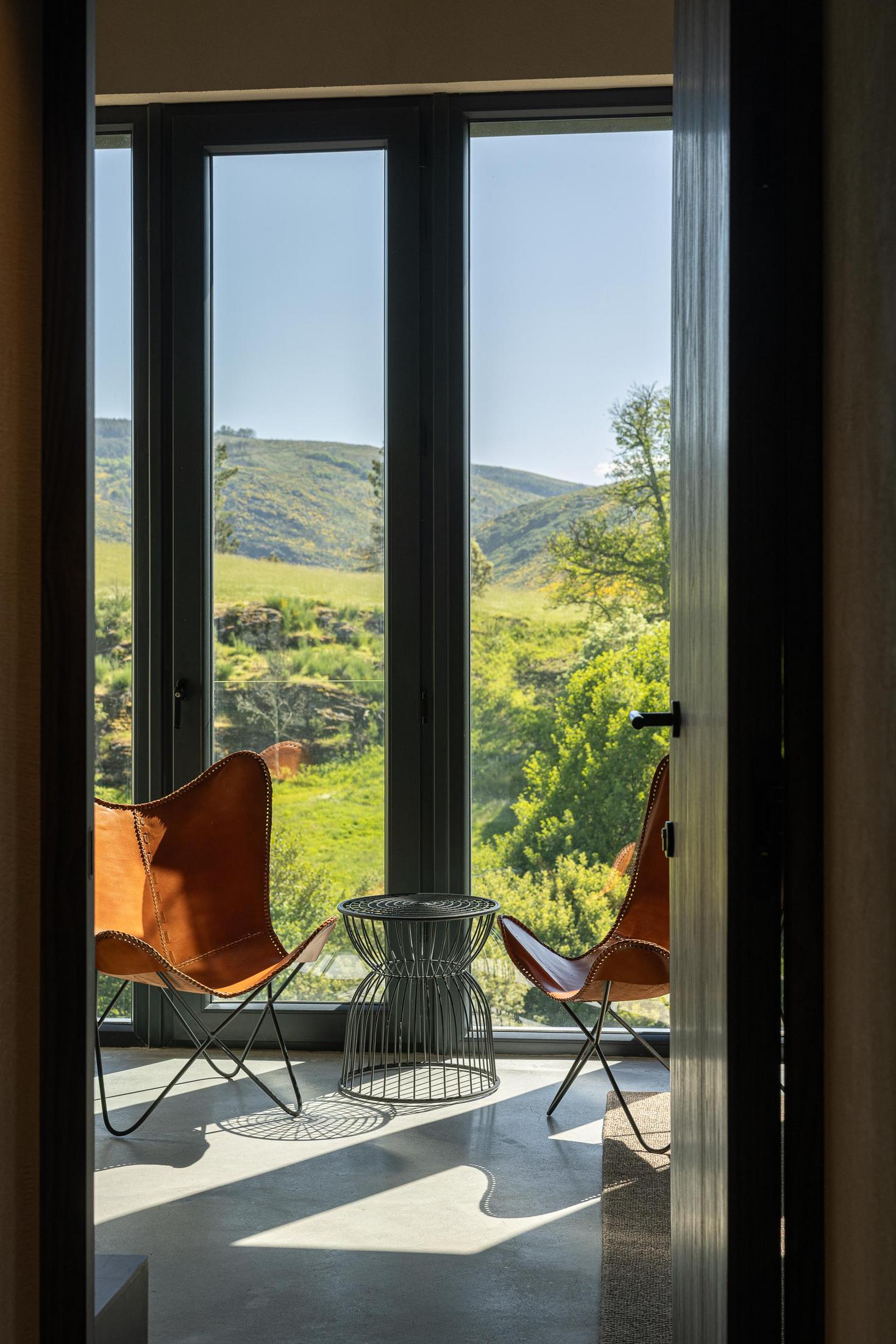 Quarto: Canto de leitura com cadeiras de pele e vista para a paisagem. — TerraSense Mountain Charm Retreat arquitetura DRK Atelier em Guarda