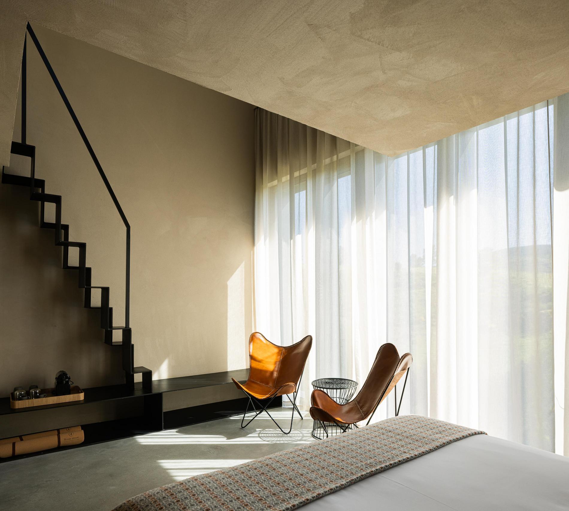 Quarto: Cama de casal com cadeiras de pele e escadas de acesso ao piso superior. — TerraSense Mountain Charm Retreat arquitetura DRK Atelier em Guarda