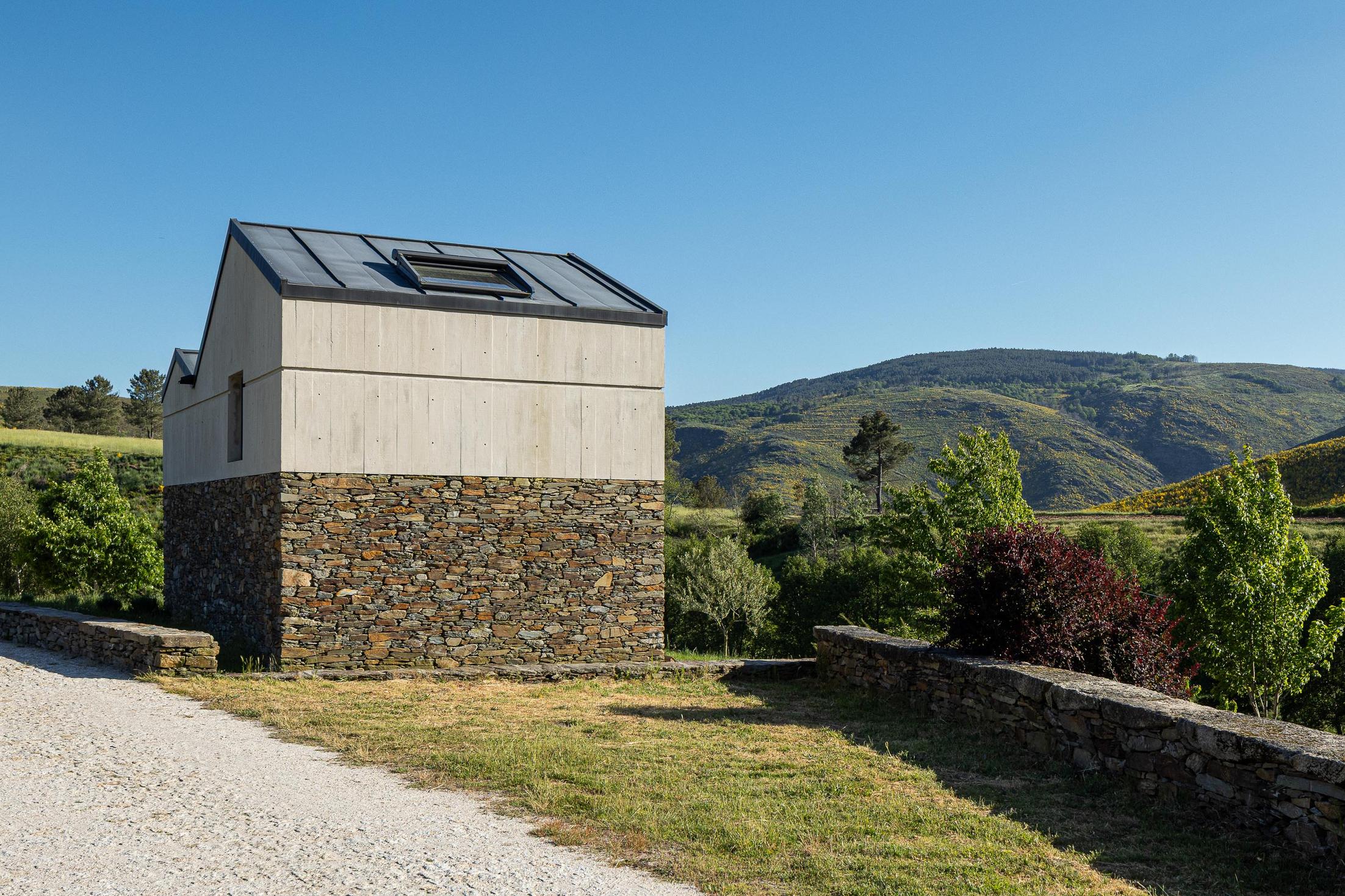 Exterior: Vista lateral da casa com revestimento em pedra e betão, e claraboia no telhado. — TerraSense Mountain Charm Retreat arquitetura DRK Atelier em Guarda