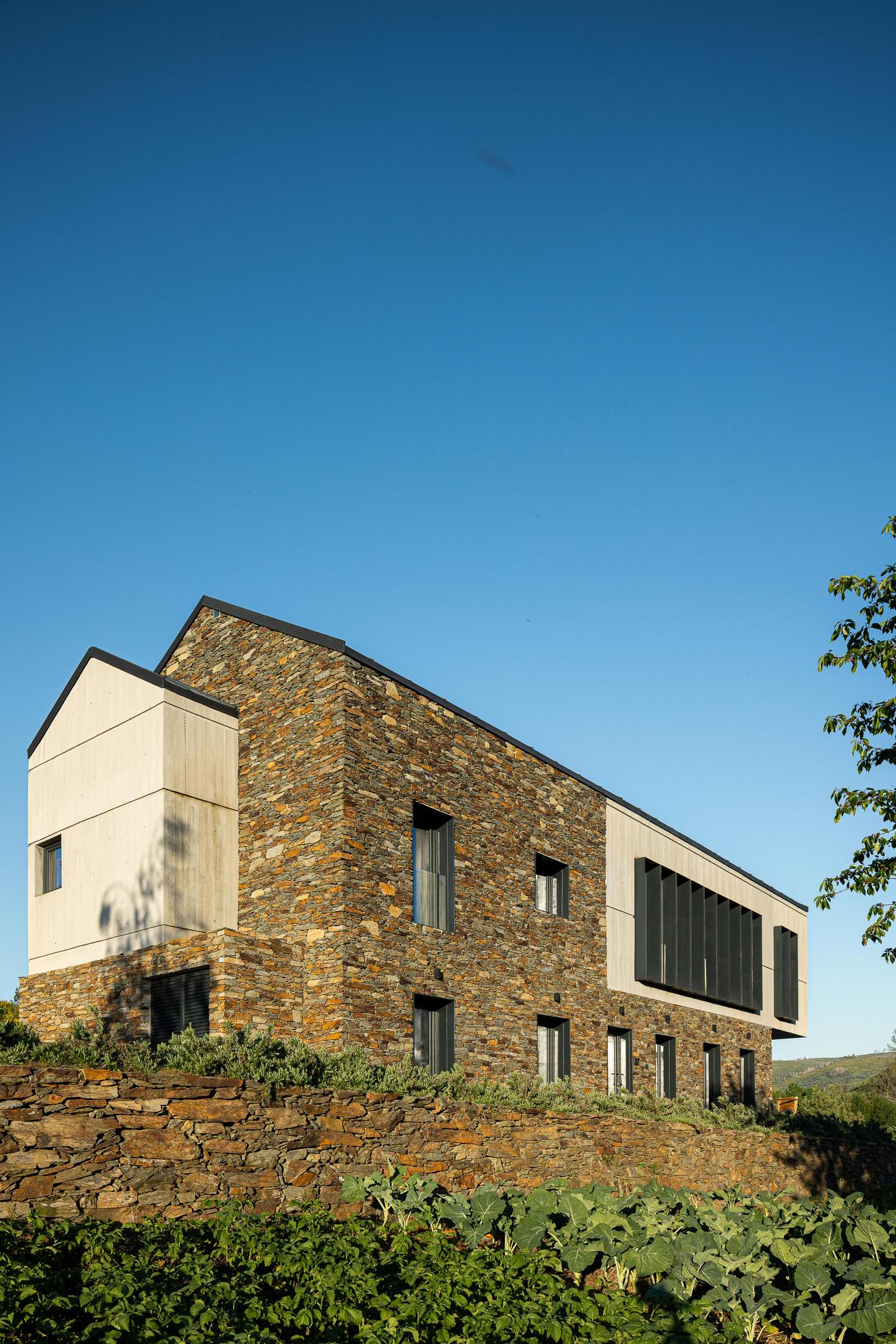 Hall de entrada: Detalhe da escada em granito, parede em pedra e painéis em madeira. — TerraSense Mountain Charm Retreat arquitetura DRK Atelier em Guarda
