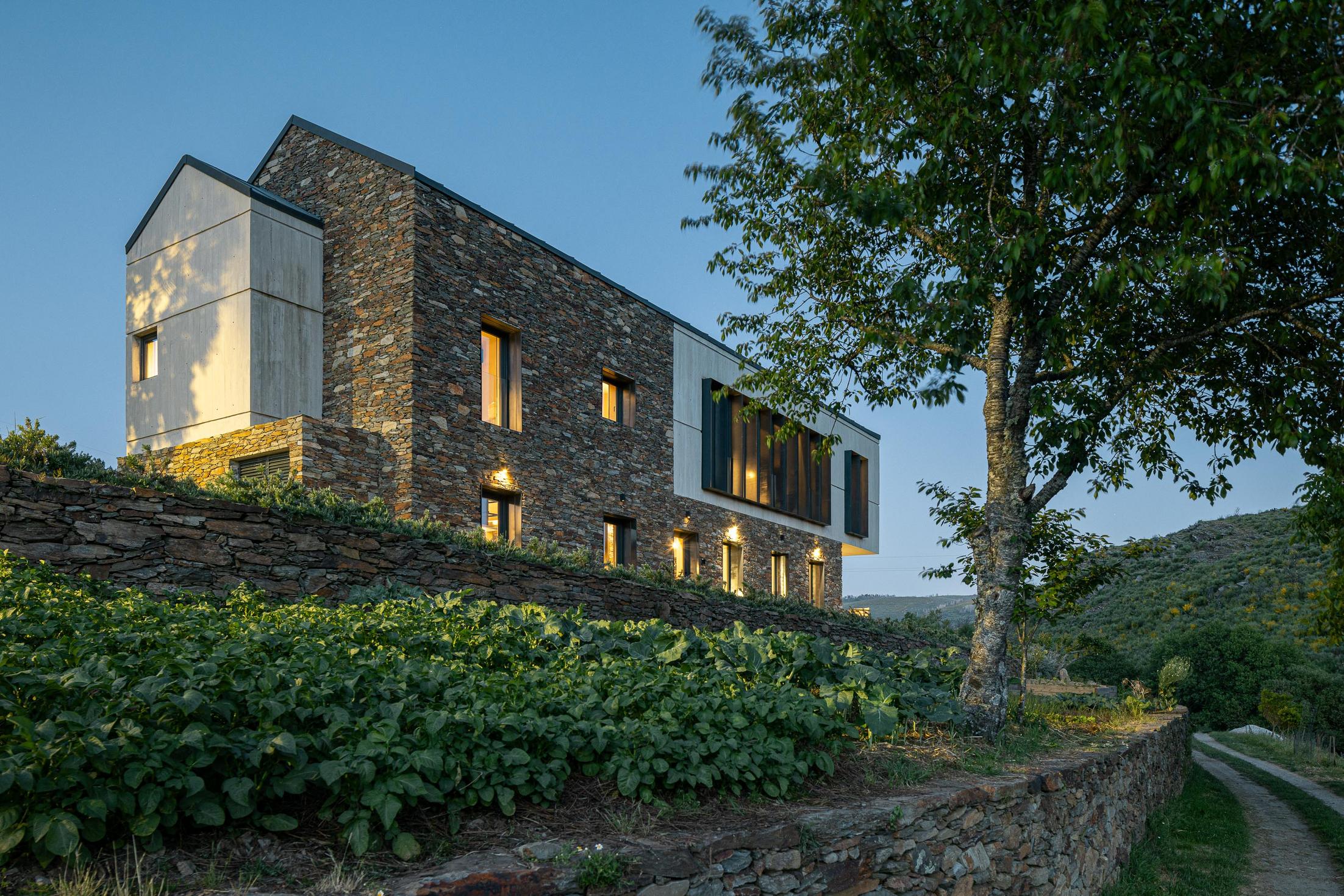 Exterior: Casa com revestimento em pedra e betão, com zona de estar exterior iluminada. — TerraSense Mountain Charm Retreat arquitetura DRK Atelier em Guarda