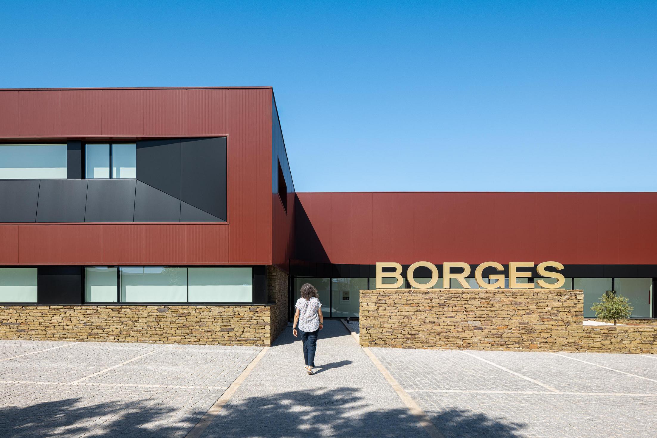 Entrada: Fachada moderna com revestimento cor de vinho e base em pedra, estacionamento em calçada portuguesa. — Adega Vinhos Borges arquitetura Em Paralelo em Vila Real