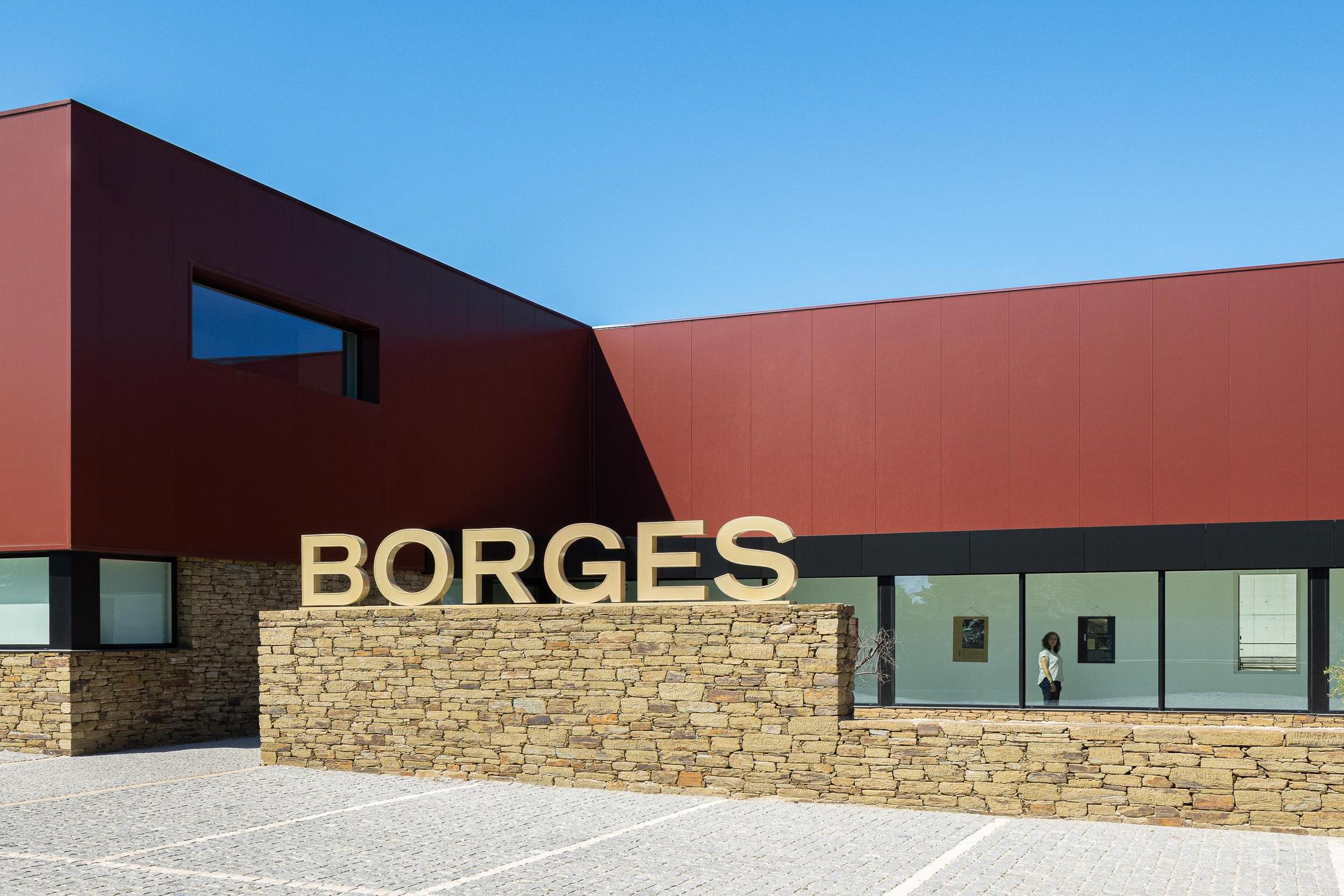Entrada: Edifício com revestimento cor de vinho e base em pedra, grandes janelas para a galeria de arte. — Adega Vinhos Borges arquitetura Em Paralelo em Vila Real