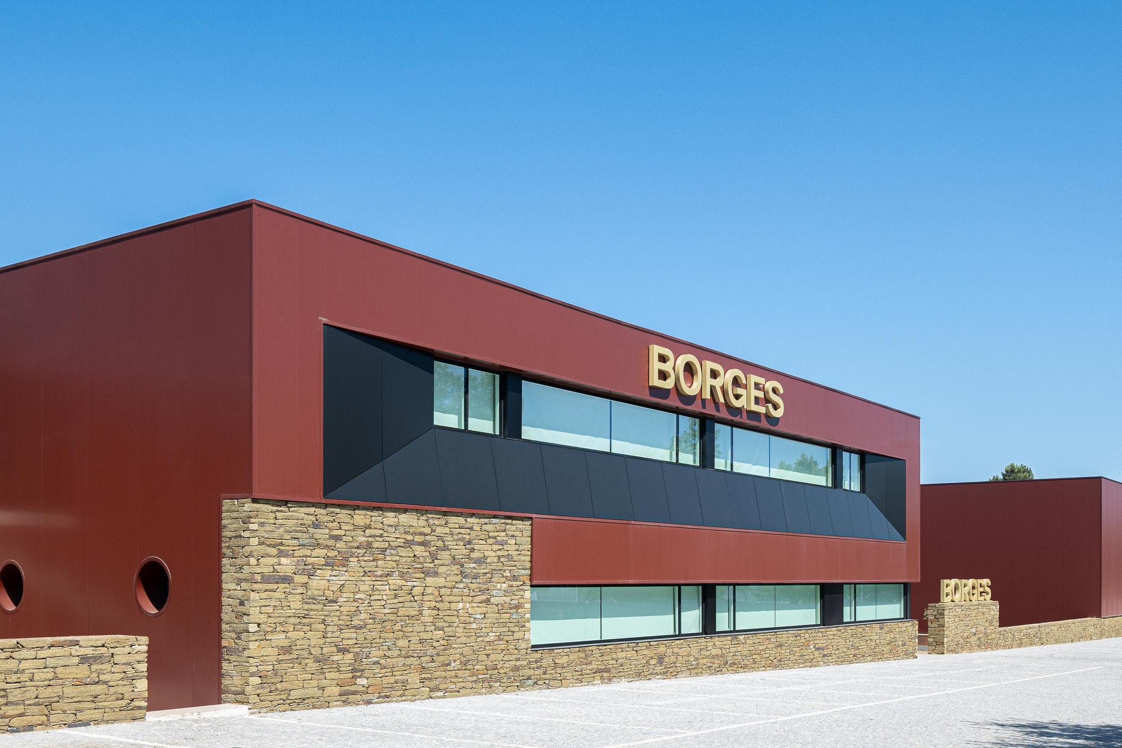 Exterior: Vista lateral do edifício com revestimento cor de vinho, detalhes em pedra e janelas circulares. — Adega Vinhos Borges arquitetura Em Paralelo em Vila Real