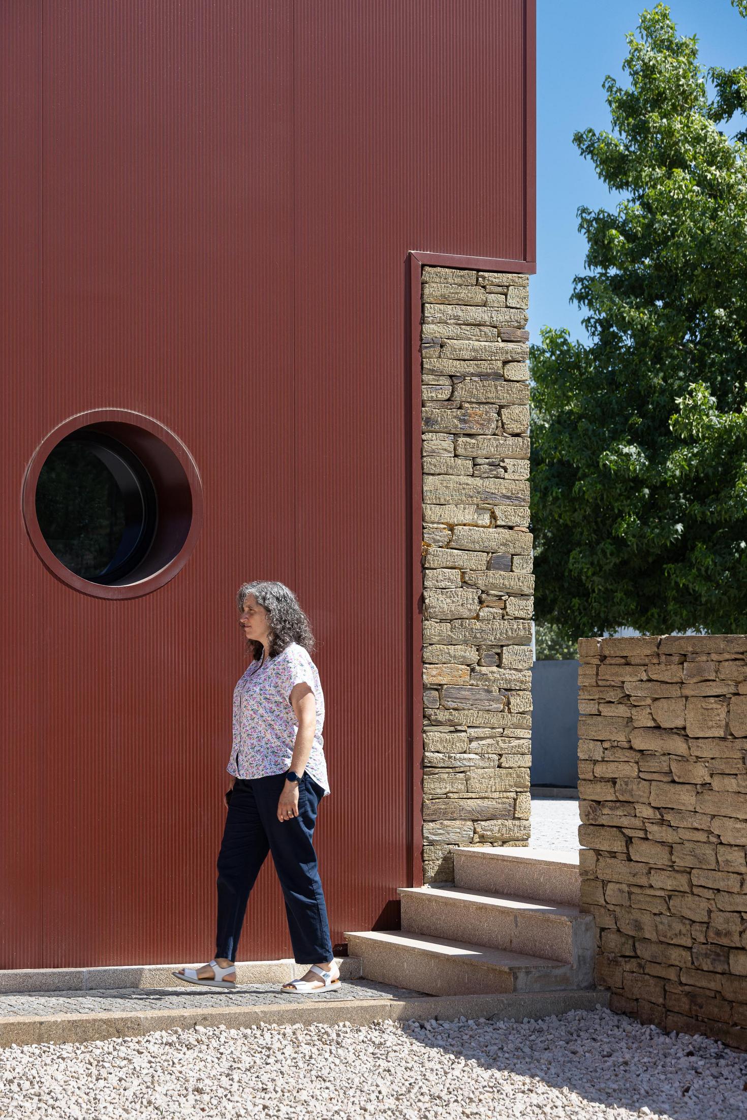 Exterior: Detalhe da fachada com revestimento cor de vinho, janela circular e escadas de acesso ao jardim. — Adega Vinhos Borges arquitetura Em Paralelo em Vila Real