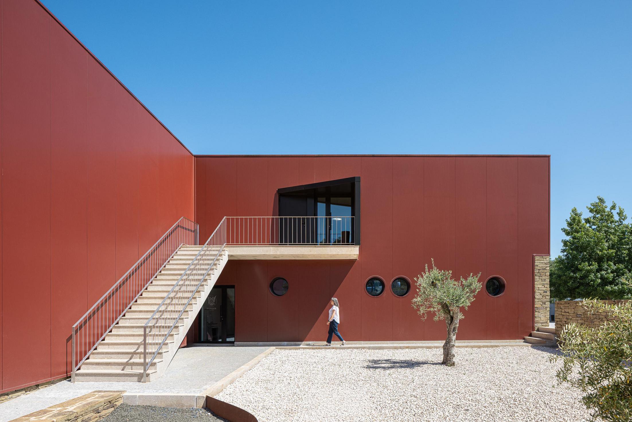 Exterior: Escadaria exterior com varanda, fachada cor de vinho com janelas circulares e oliveira. — Adega Vinhos Borges arquitetura Em Paralelo em Vila Real