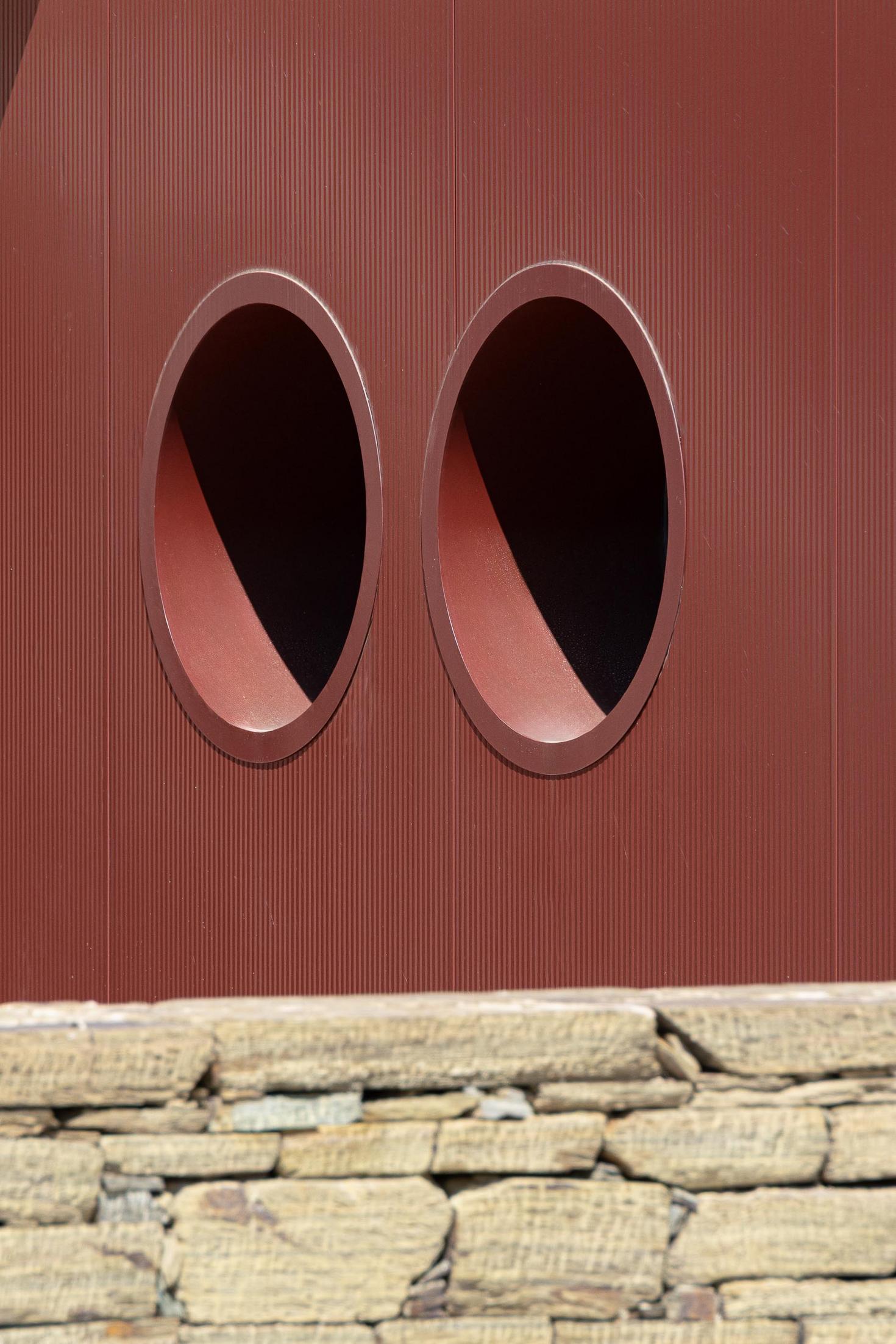 Exterior: Detalhe de duas janelas circulares na fachada com revestimento cor de vinho e muro de pedra. — Adega Vinhos Borges arquitetura Em Paralelo em Vila Real
