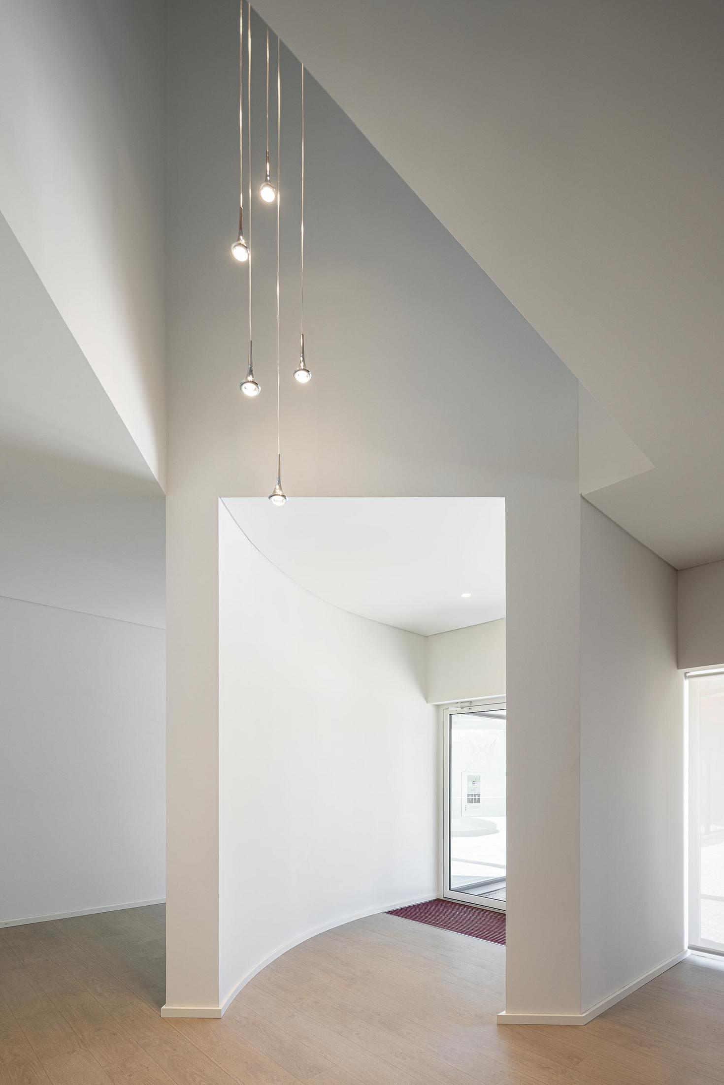 Hall: Hall de entrada com candeeiros pendentes, paredes brancas e pavimento em madeira clara. — Adega Vinhos Borges arquitetura Em Paralelo em Vila Real