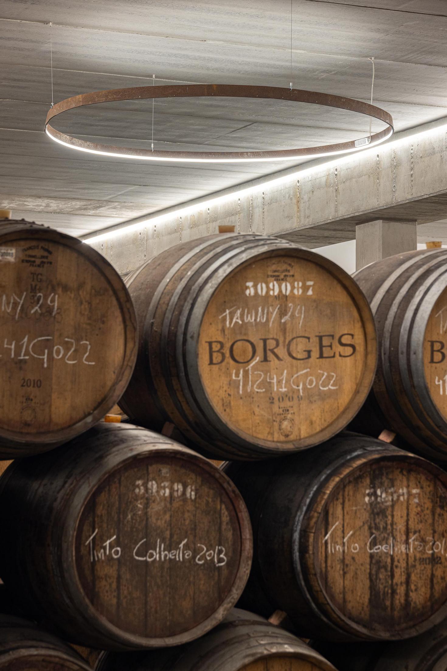 Cave: Detalhe das barricas de vinho com a inscrição "BORGES" e candeeiro circular suspenso. — Adega Vinhos Borges arquitetura Em Paralelo em Vila Real
