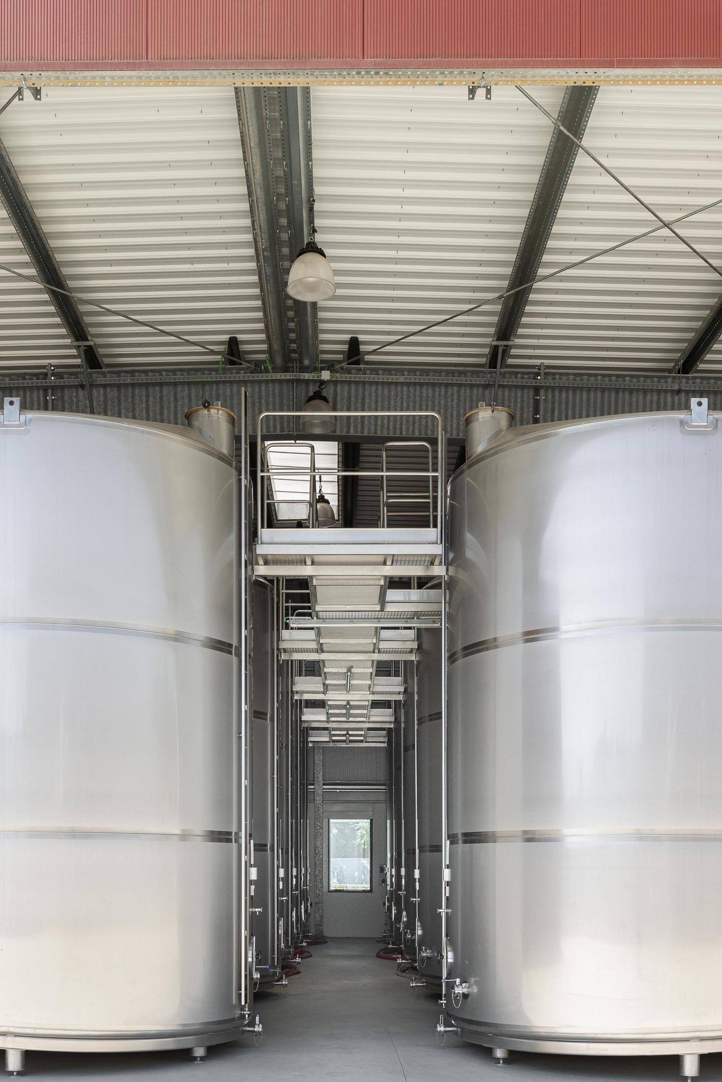 Zona de produção: Tanques de inox alinhados com passadiços e escadas de acesso. — Adega Vinhos Borges arquitetura Em Paralelo em Vila Real
