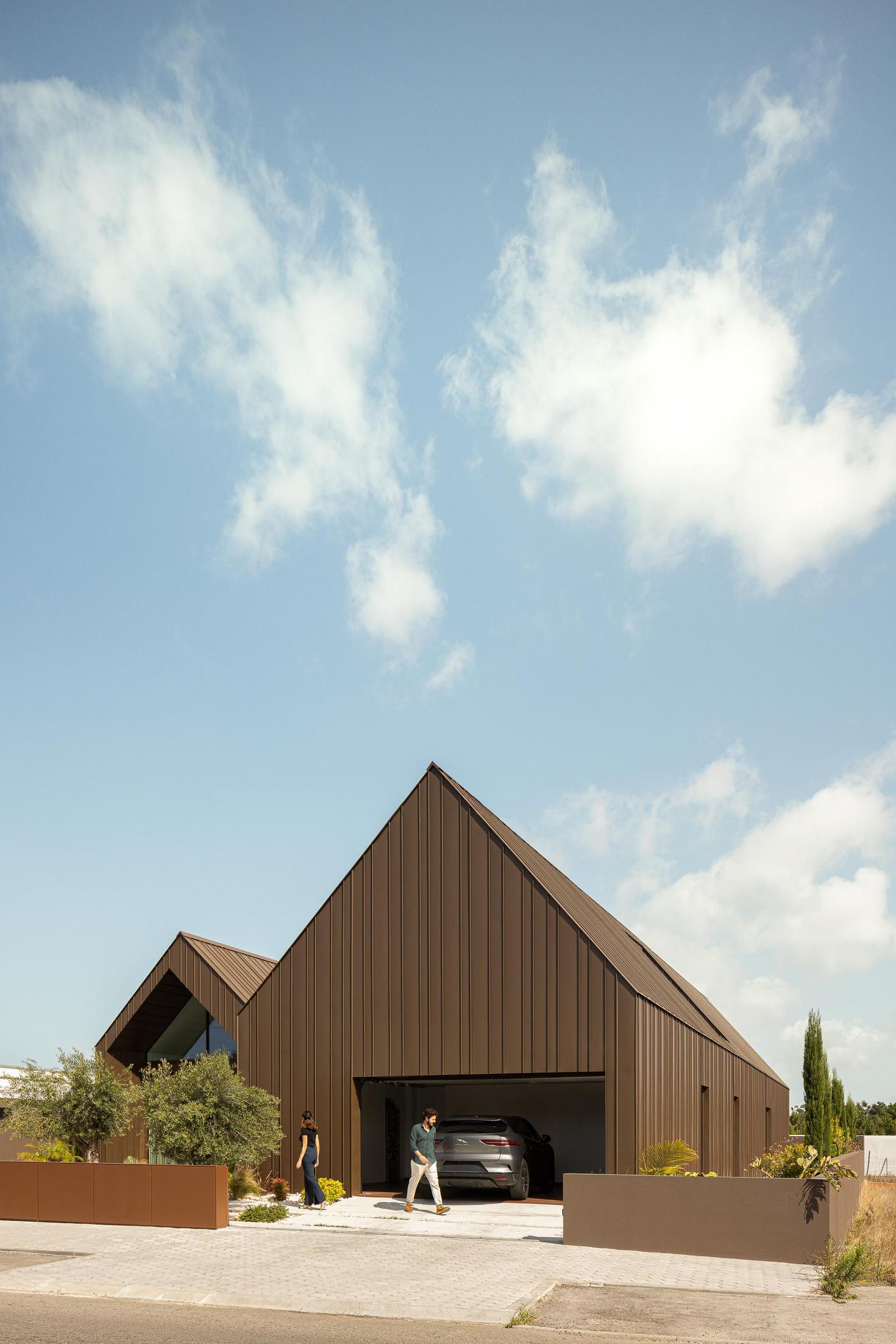 Exterior: Vista frontal da casa com garagem aberta e revestimento metálico castanho. — House SM arquitetura Mário Alves Arquitecto em Ílhavo