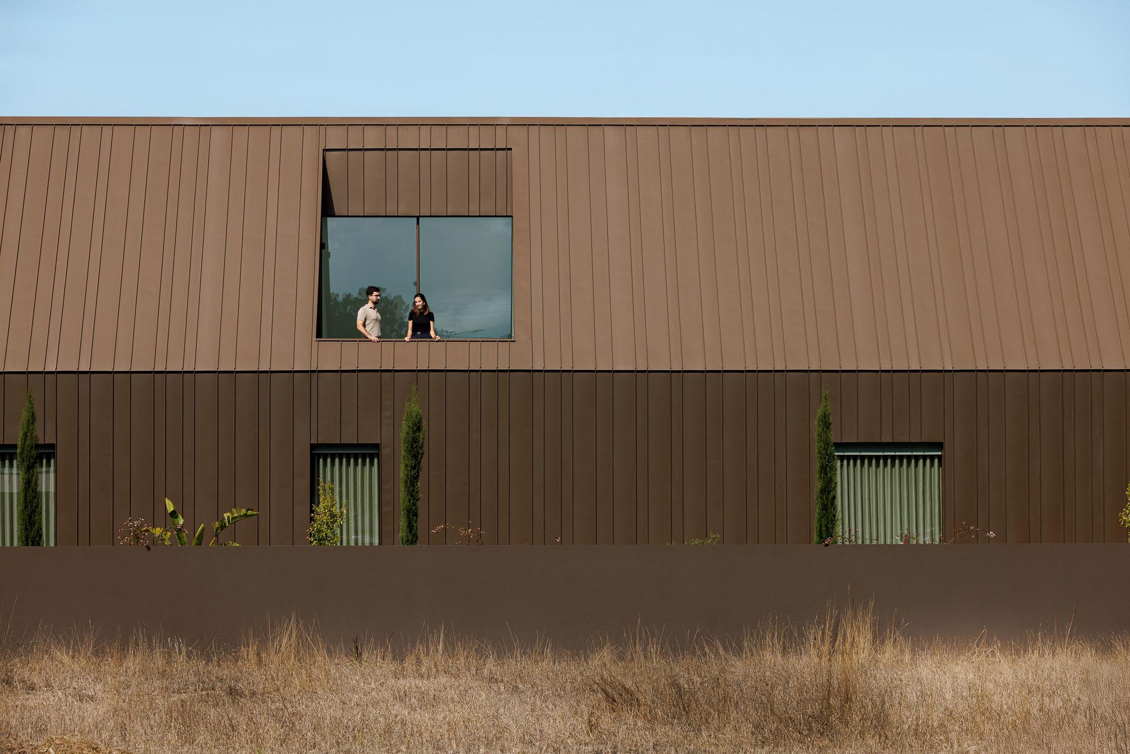 Exterior: Fachada posterior da casa com revestimento metálico castanho e janelas. — House SM arquitetura Mário Alves Arquitecto em Ílhavo