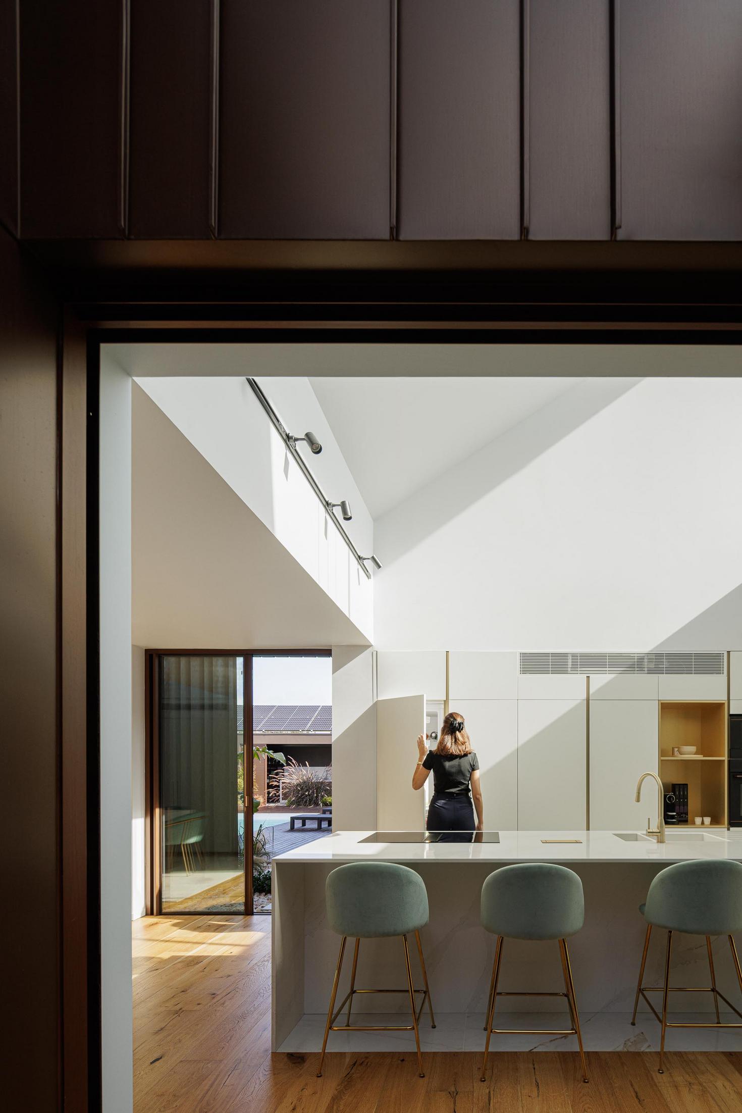 Cozinha: Ilha em pedra clara com lavatório dourado, armários brancos e cadeiras turquesa. — House SM arquitetura Mário Alves Arquitecto em Ílhavo