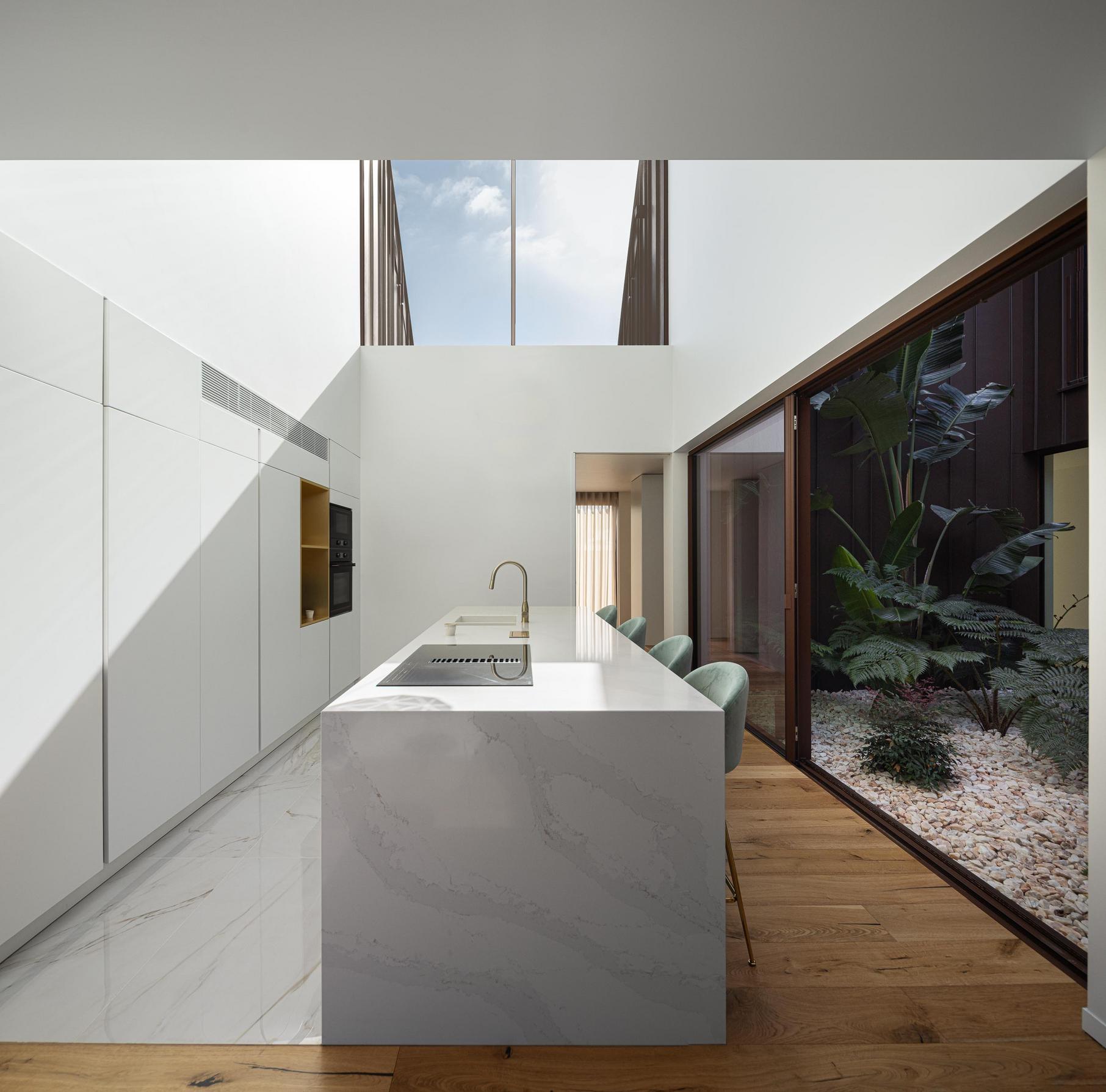 Cozinha: Ilha em pedra clara, pavimento em madeira e vista para pátio interior. — House SM arquitetura Mário Alves Arquitecto em Ílhavo
