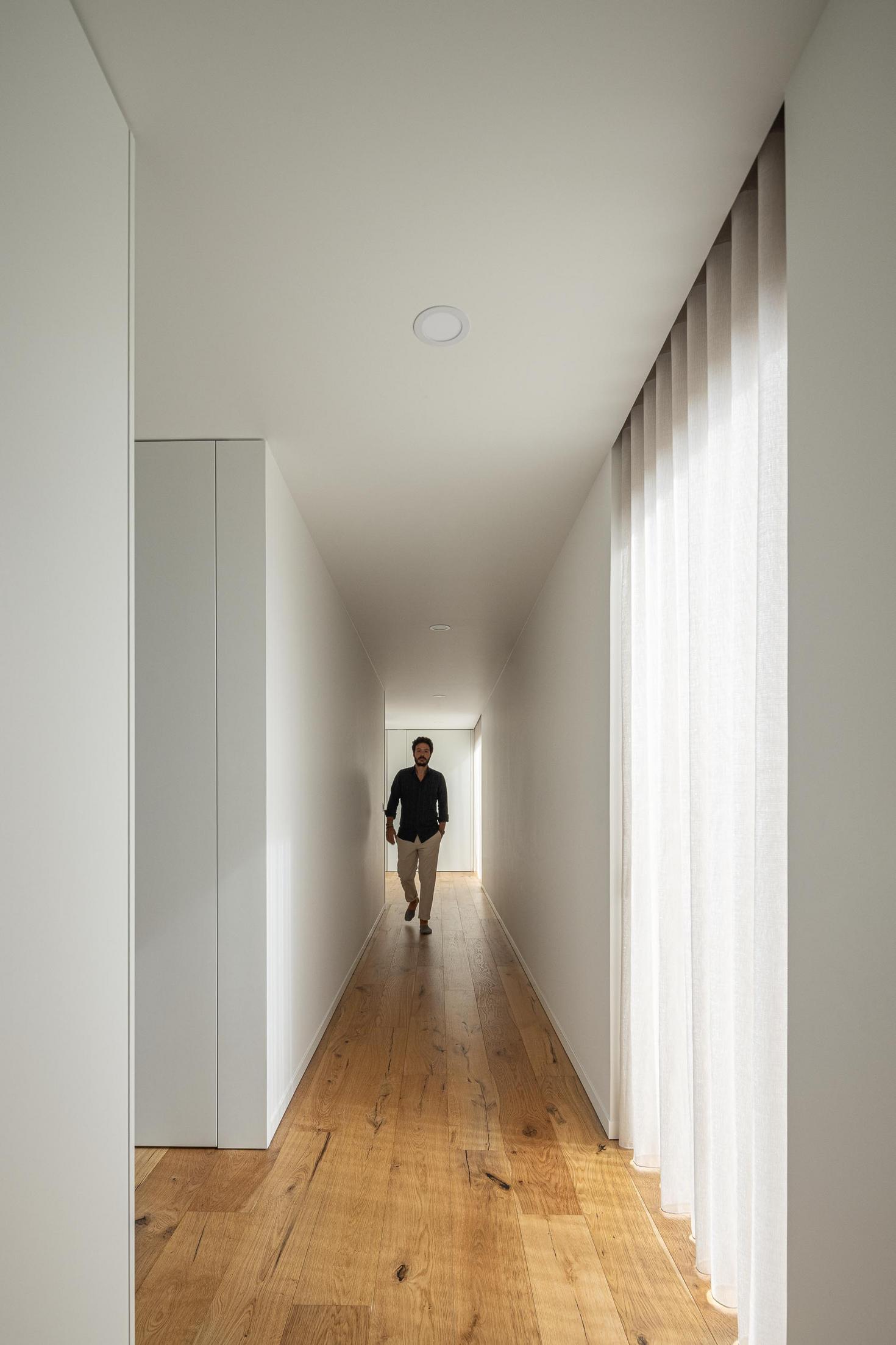 Corredor: Corredor branco com pavimento em madeira e cortina clara. — House SM arquitetura Mário Alves Arquitecto em Ílhavo