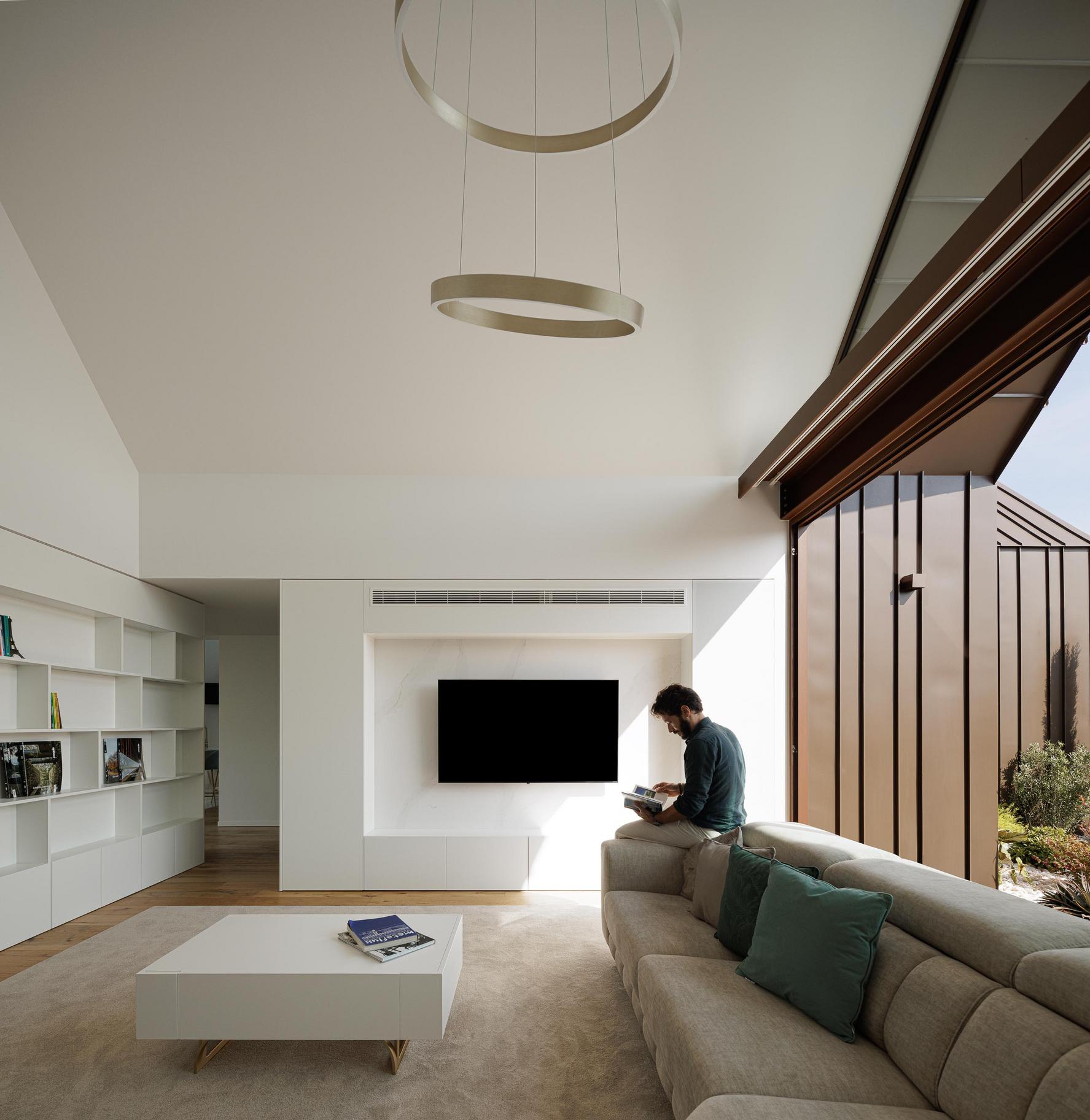 Sala de estar: Sofá cinzento, mesa branca, estante e televisão. — House SM arquitetura Mário Alves Arquitecto em Ílhavo