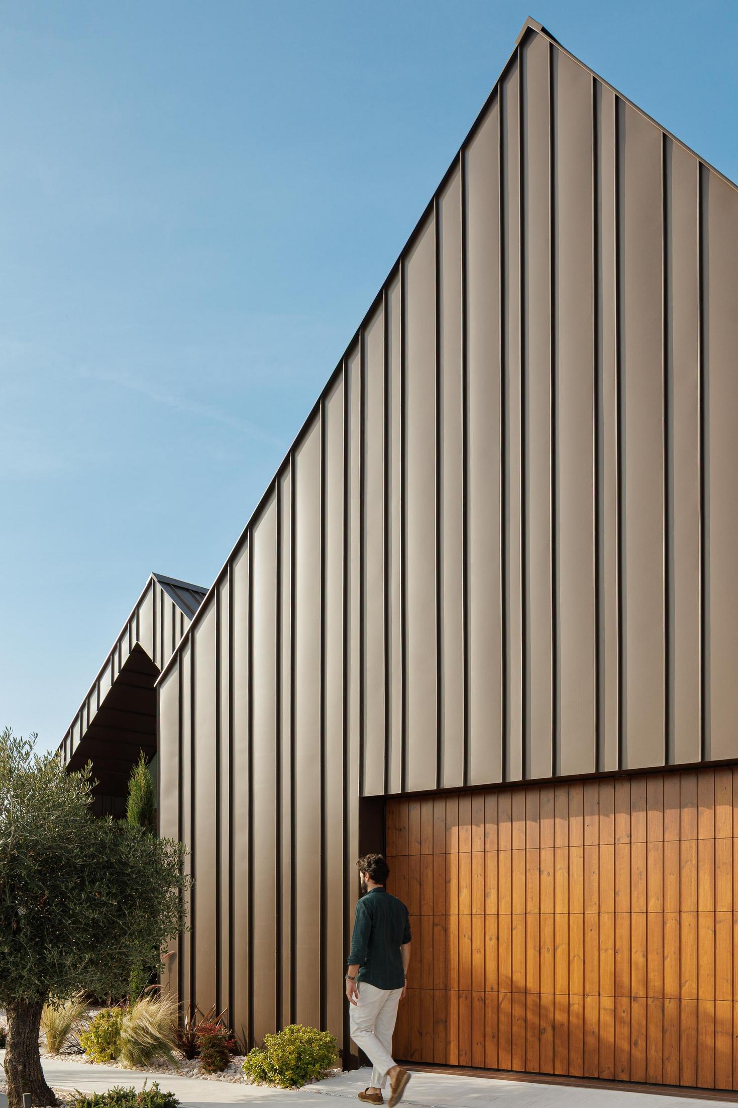 Exterior: Detalhe da fachada com porta da garagem em madeira e revestimento metálico castanho. — House SM arquitetura Mário Alves Arquitecto em Ílhavo