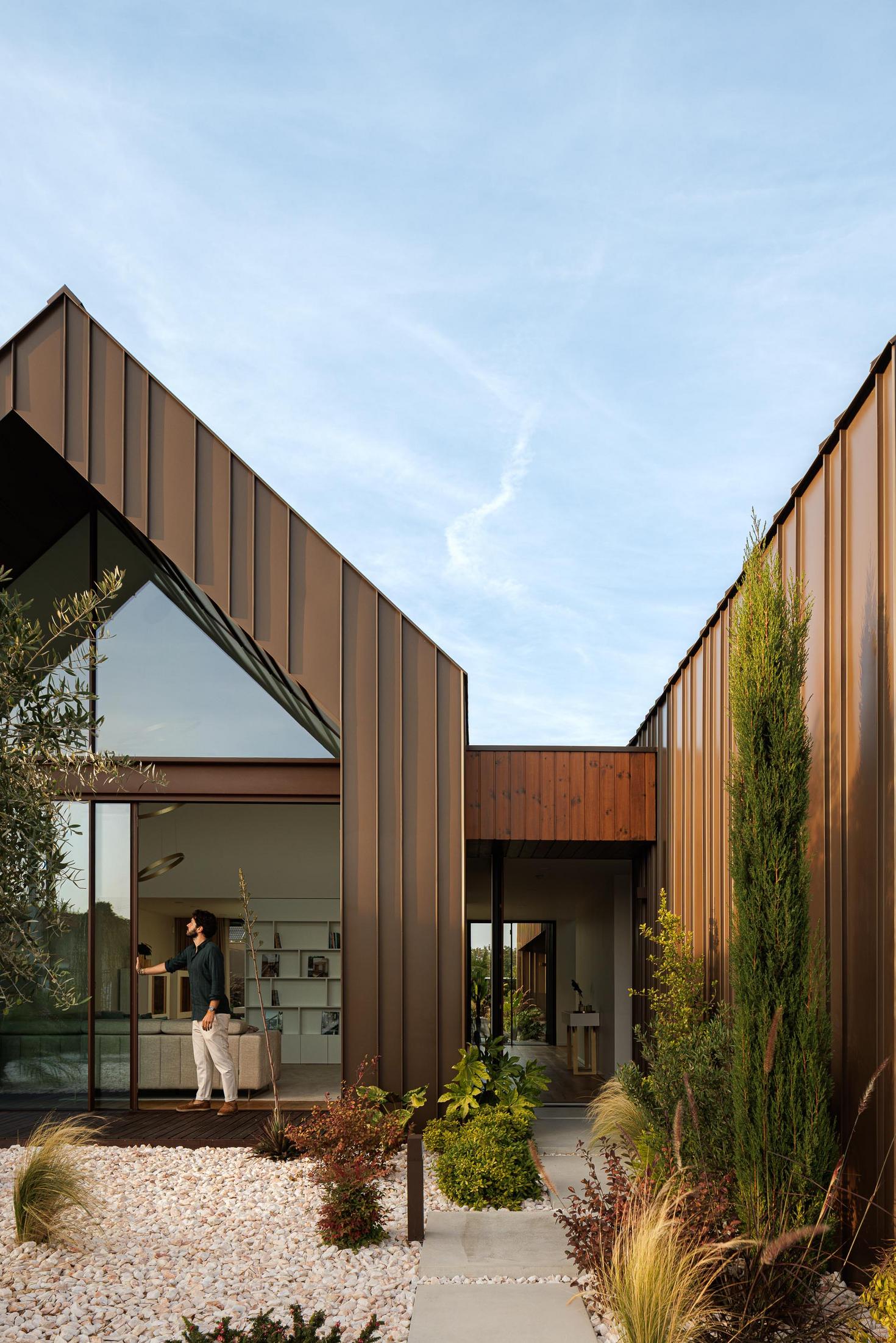Entrada: Vista da entrada com vegetação, revestimento metálico e porta de vidro. — House SM arquitetura Mário Alves Arquitecto em Ílhavo
