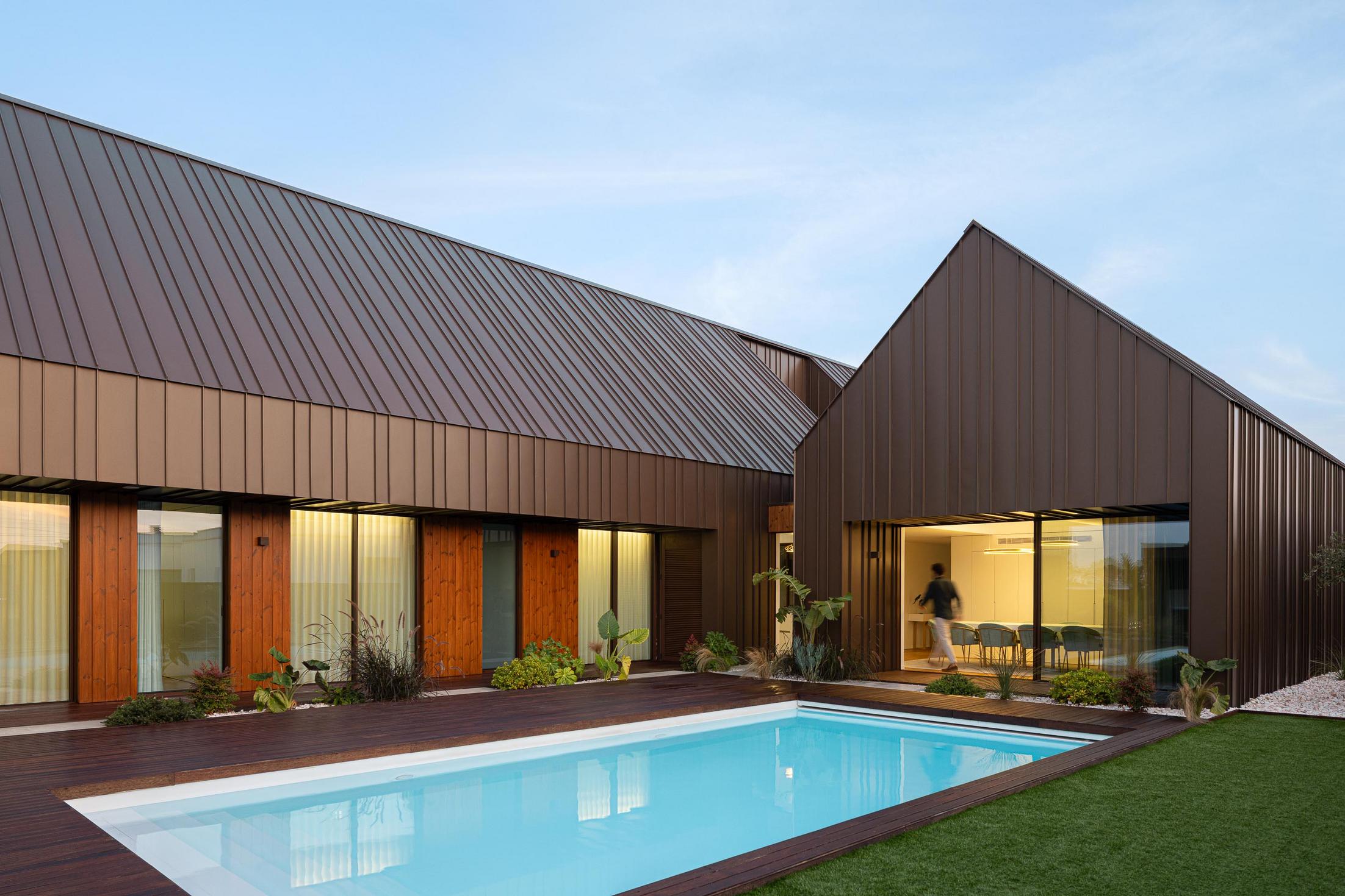 Exterior: Piscina com deck em madeira e vista para a fachada da casa ao entardecer. — House SM arquitetura Mário Alves Arquitecto em Ílhavo