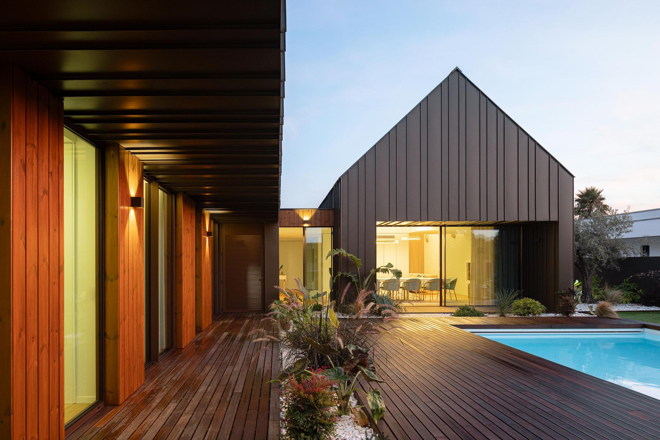 Exterior: Piscina com deck em madeira e vista para a sala de jantar iluminada. — House SM arquitetura Mário Alves Arquitecto em Ílhavo