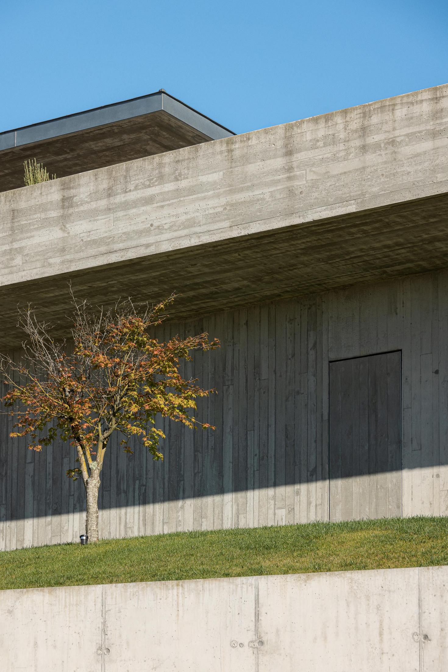 Exterior: Vista aérea da casa moderna em betão, integrada na encosta, com piscina e relvado. — CASA A arquitetura L2C Arquitetura em Braga