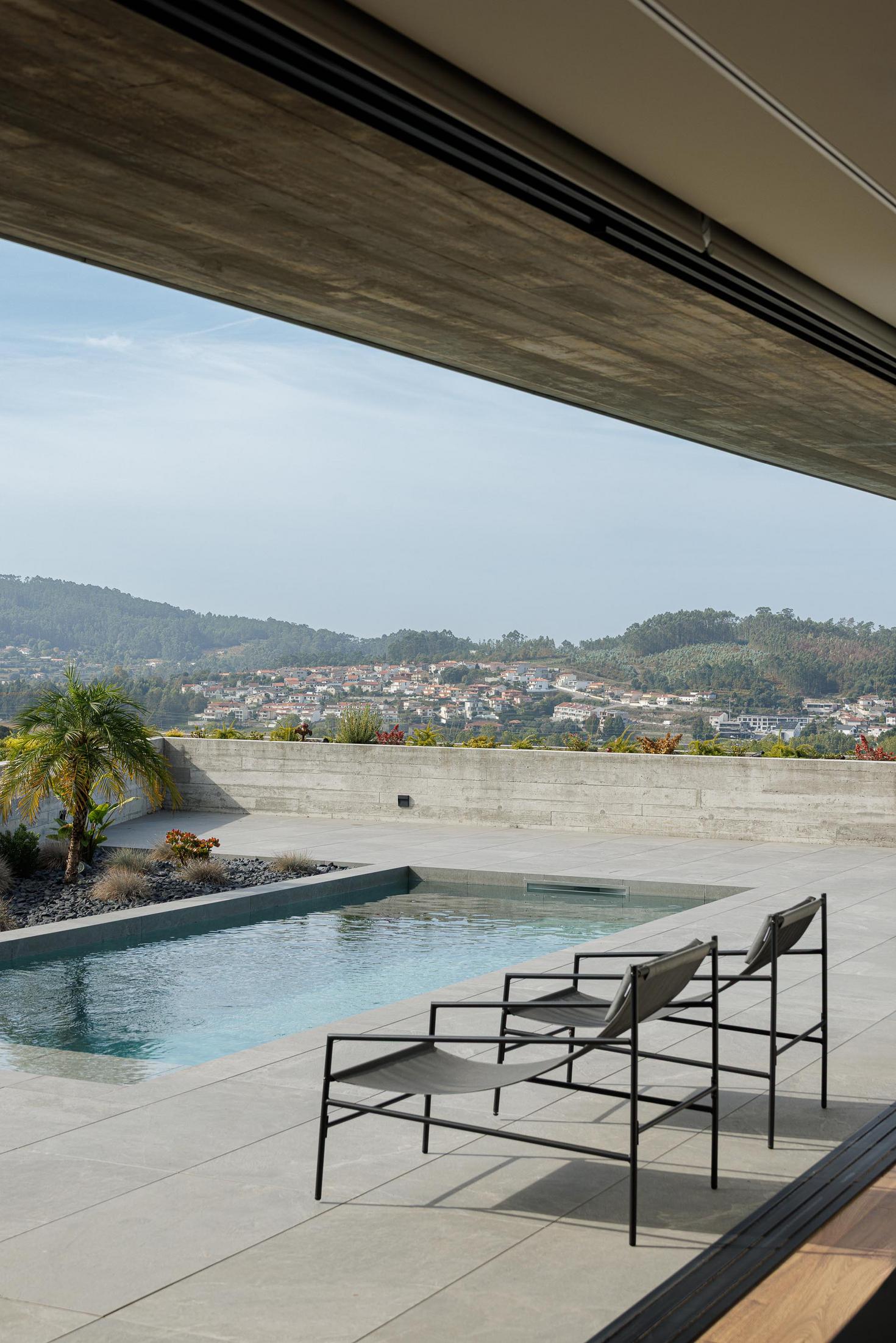 Exterior: Alpendre com piscina e vista para a paisagem, com homem a entrar na sala. — CASA A arquitetura L2C Arquitetura em Braga