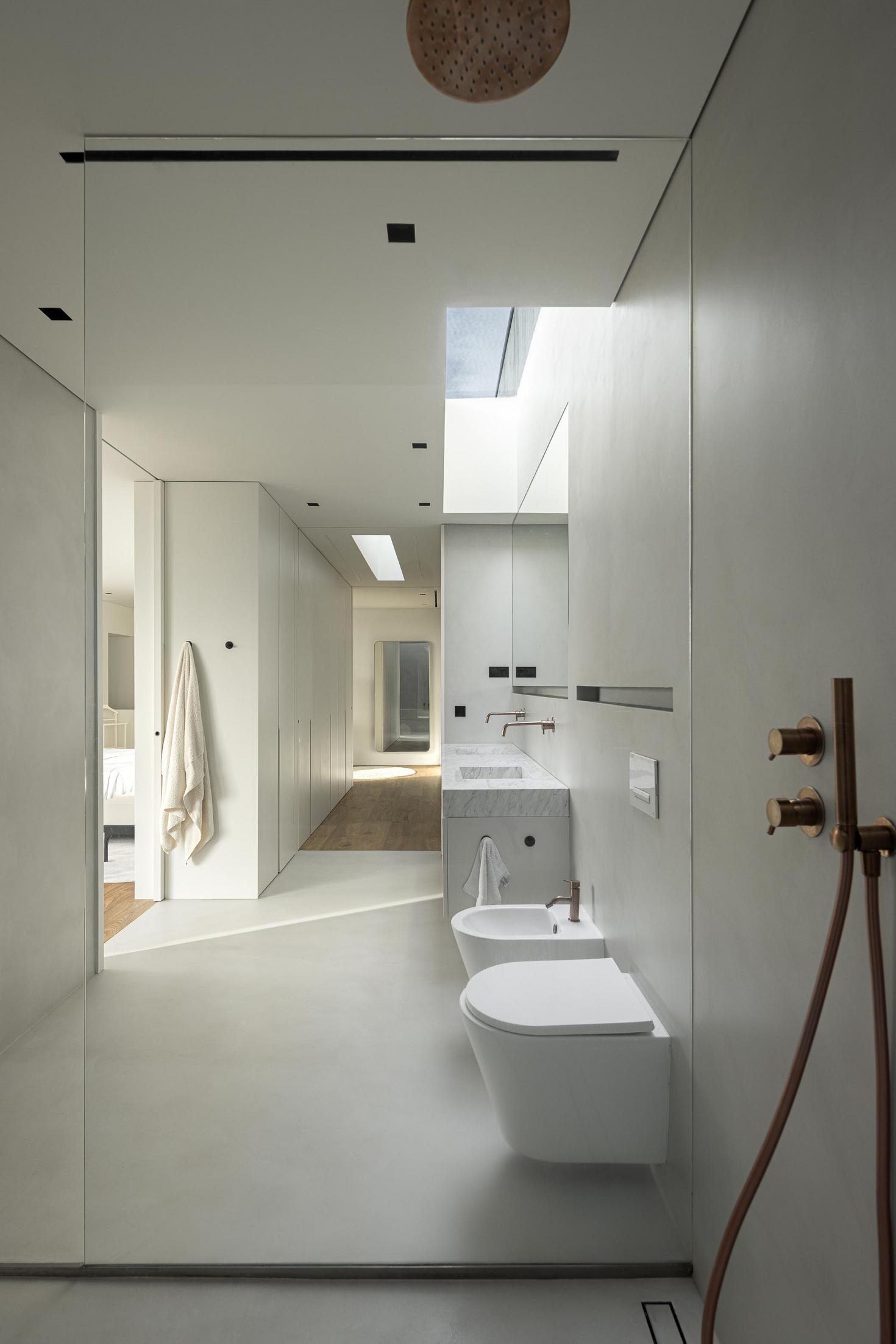 Casa de banho: Lavatório duplo em mármore, sanita suspensa e iluminação indireta. — CASA A arquitetura L2C Arquitetura em Braga
