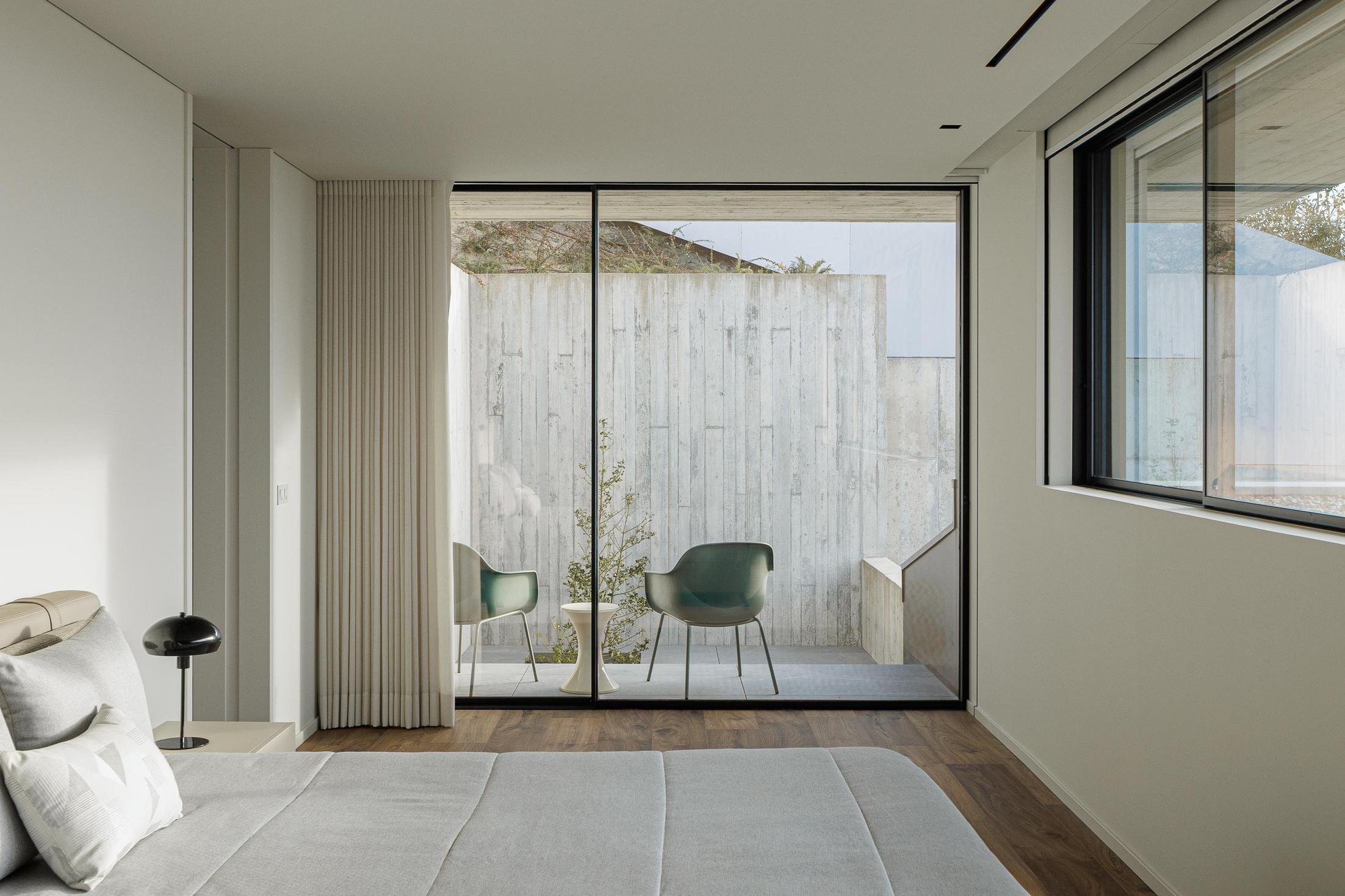 Quarto: Detalhe da mesa de cabeceira com candeeiro e acesso à casa de banho com toalha pendurada. — CASA A arquitetura L2C Arquitetura em Braga