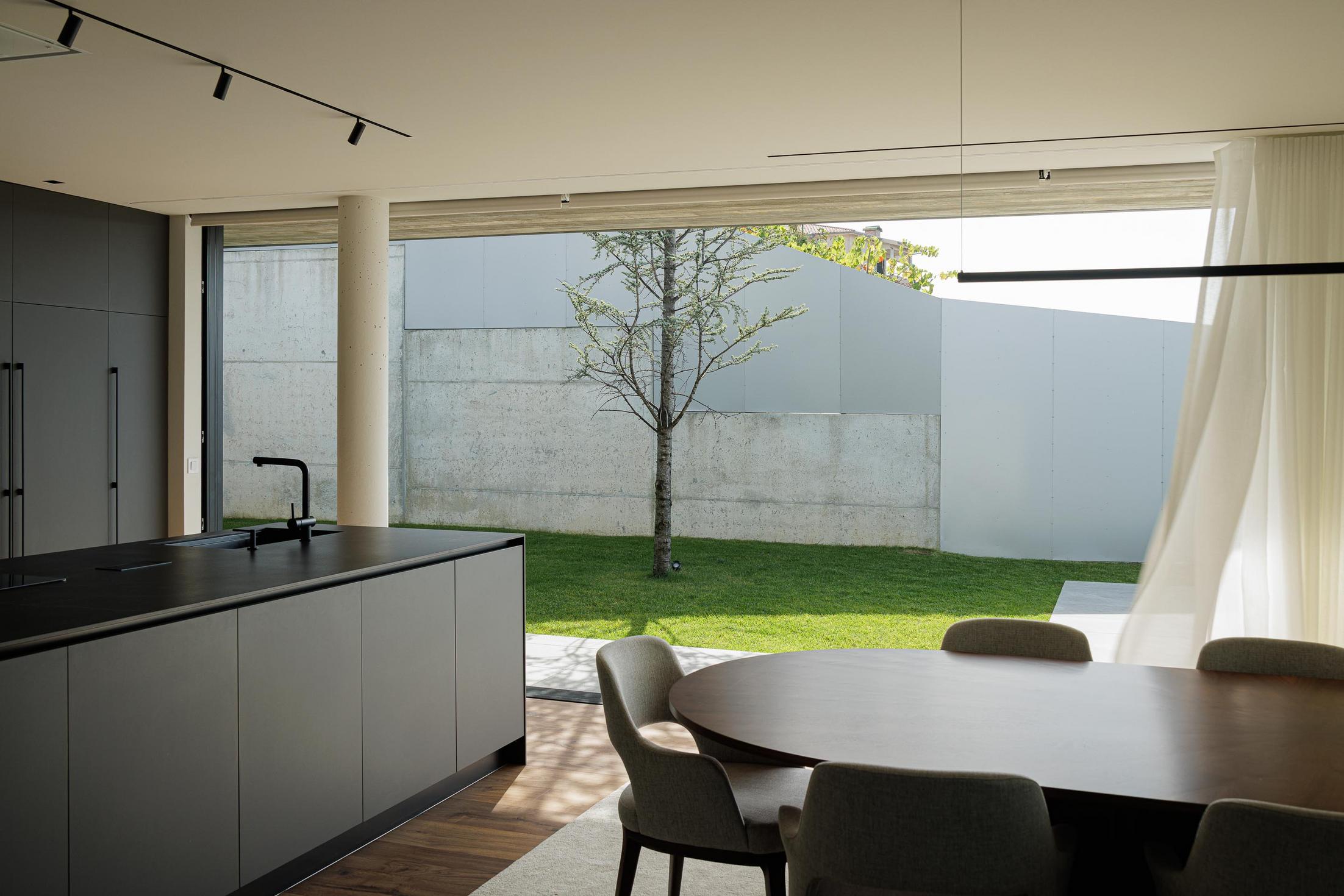 Quarto: Cama com vista para o pátio exterior com cadeiras e paredes em betão aparente. — CASA A arquitetura L2C Arquitetura em Braga
