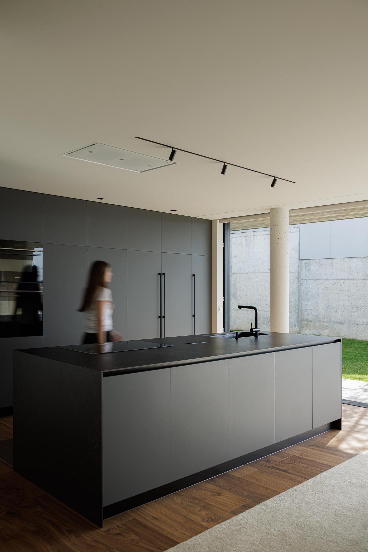 Cozinha/Sala de jantar: Ilha central escura, mesa de jantar redonda e vista para o jardim. — CASA A arquitetura L2C Arquitetura em Braga