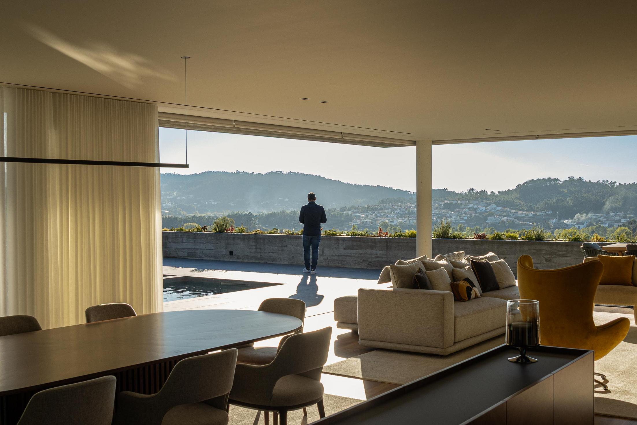 Sala de jantar: Mesa oval em madeira com cadeiras estofadas, alcatifa clara e cortinas brancas. — CASA A arquitetura L2C Arquitetura em Braga