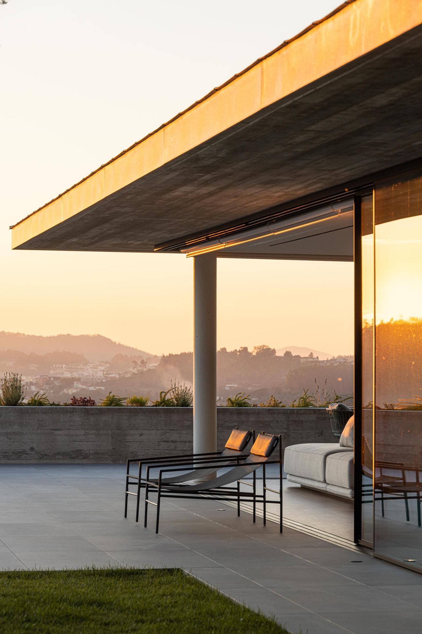 Exterior: Vista geral do pátio com piscina, relvado e fachada em betão aparente ao pôr do sol. — CASA A arquitetura L2C Arquitetura em Braga