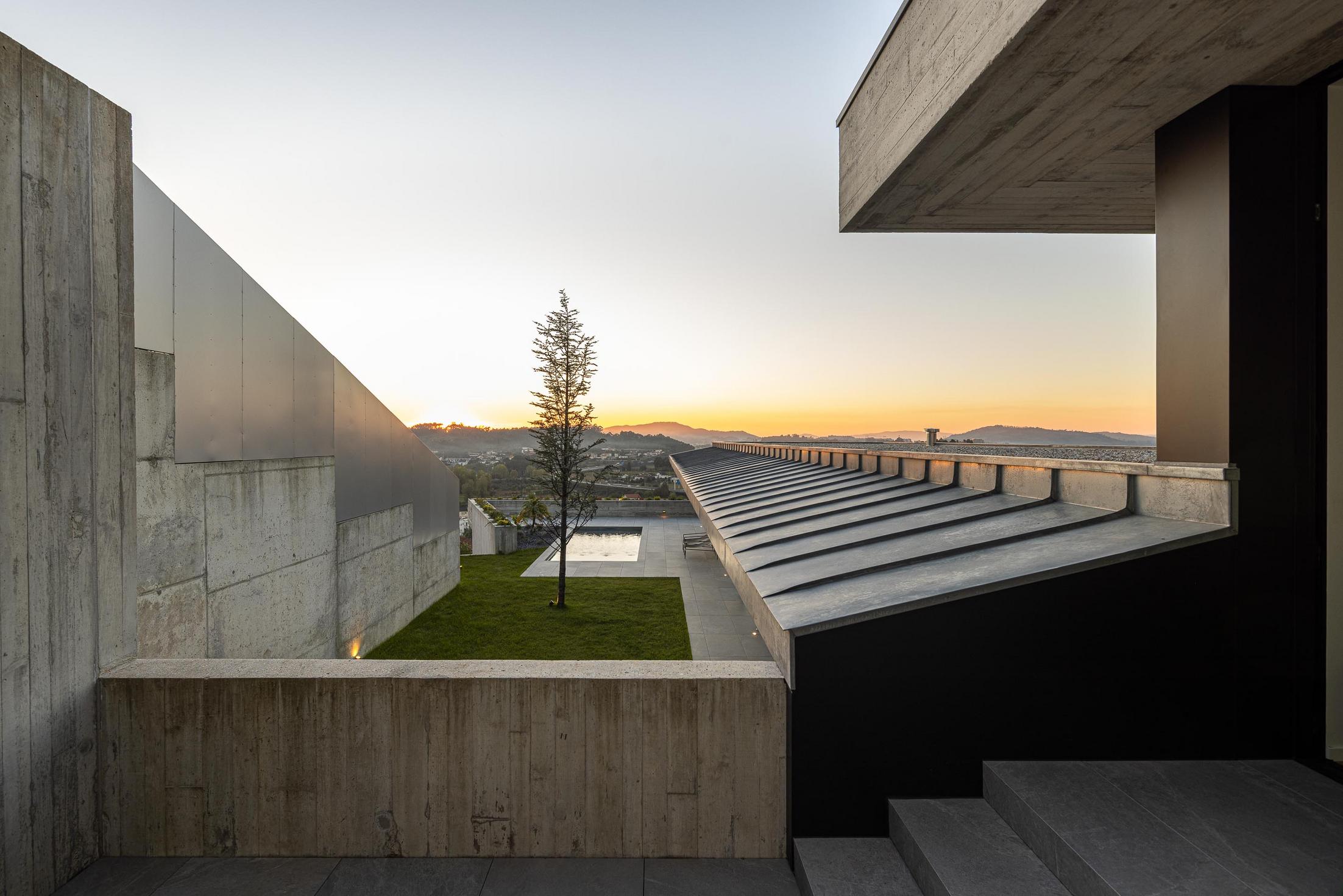 Exterior: Alpendre com sala de estar e jantar, com vista para a piscina ao entardecer. — CASA A arquitetura L2C Arquitetura em Braga