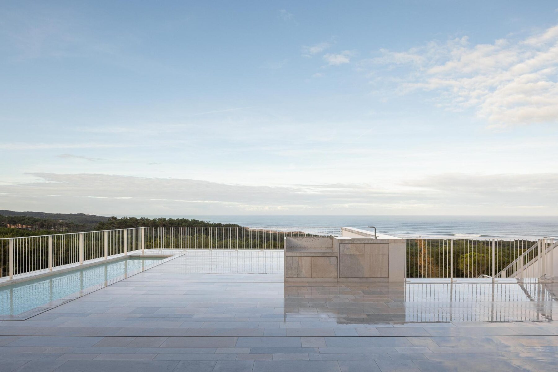 Piscina: Vista panorâmica da piscina com grade branca e oceano ao fundo, num dia soalheiro. — WEST CLIFFS D45 arquitetura ARX Portugal - Arquitectos em Óbidos