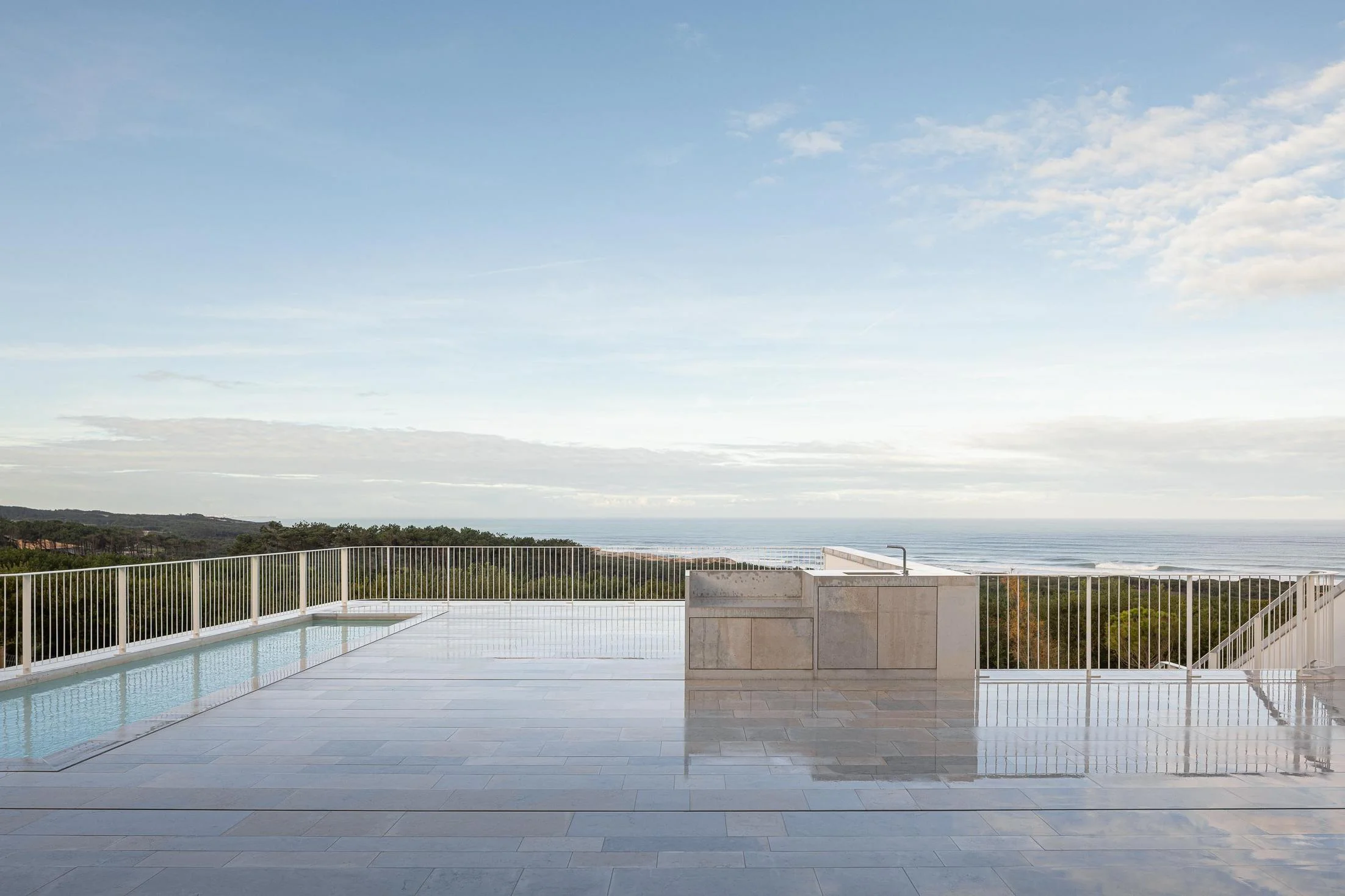 Piscina: Vista panorâmica da piscina com grade branca e oceano ao fundo, num dia soalheiro. — WEST CLIFFS D45 arquitetura ARX Portugal - Arquitectos em Óbidos