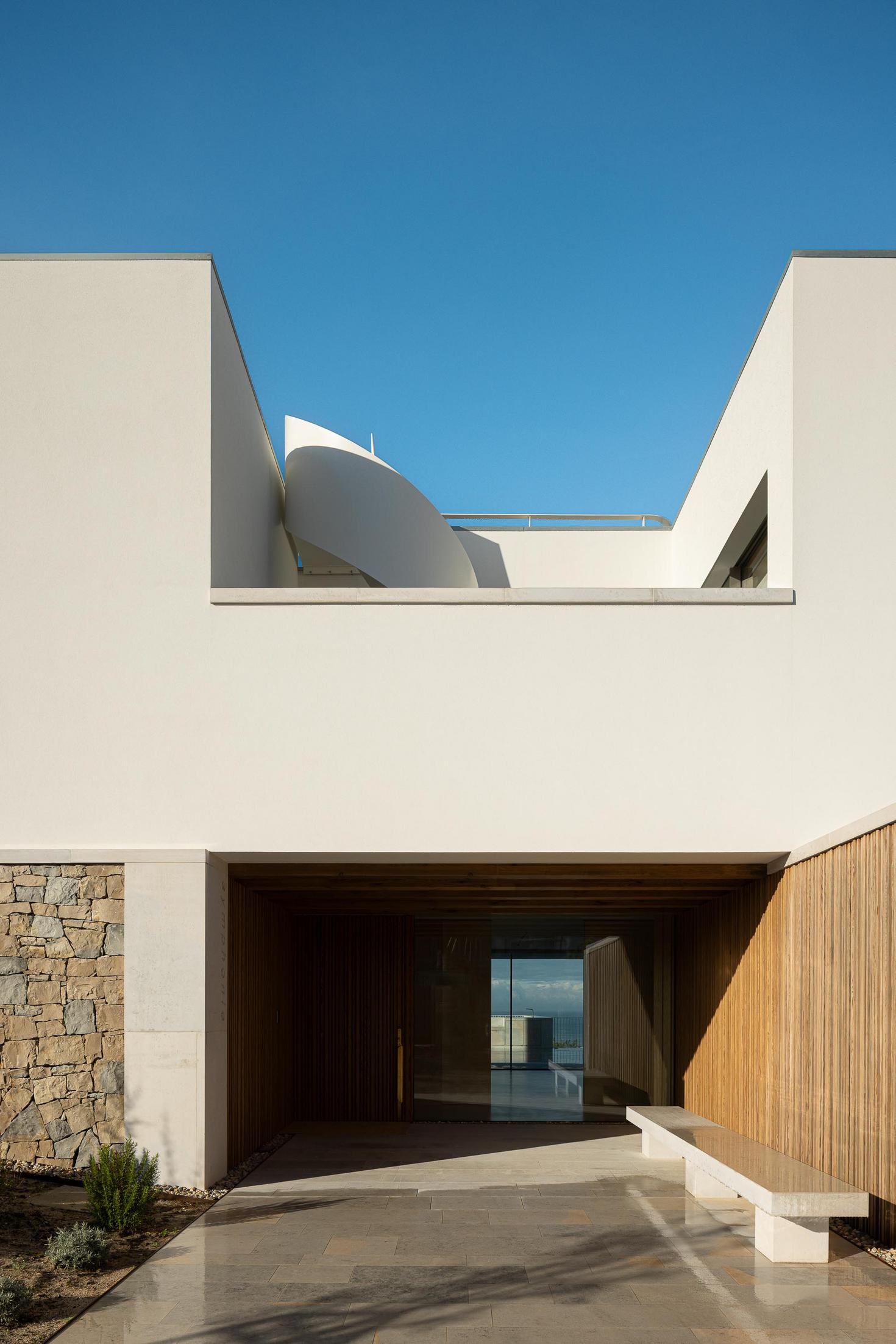 Entrada principal: Fachada frontal com porta de entrada, banco em pedra e escada exterior em espiral. — WEST CLIFFS D45 arquitetura ARX Portugal - Arquitectos em Óbidos
