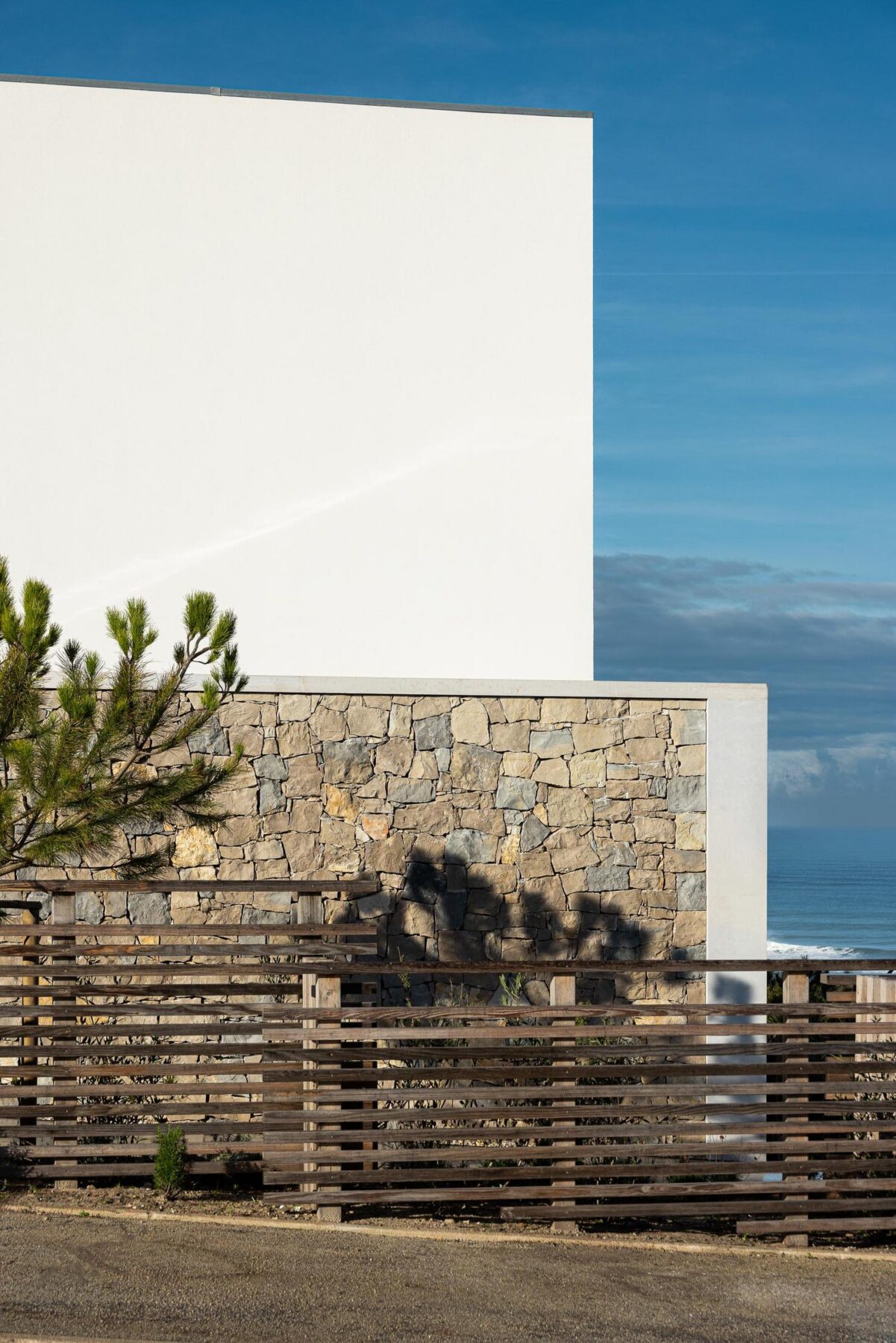 Fachada lateral: Detalhe da fachada com pedra, reboco branco e vedação de madeira horizontal. — WEST CLIFFS D45 arquitetura ARX Portugal - Arquitectos em Óbidos