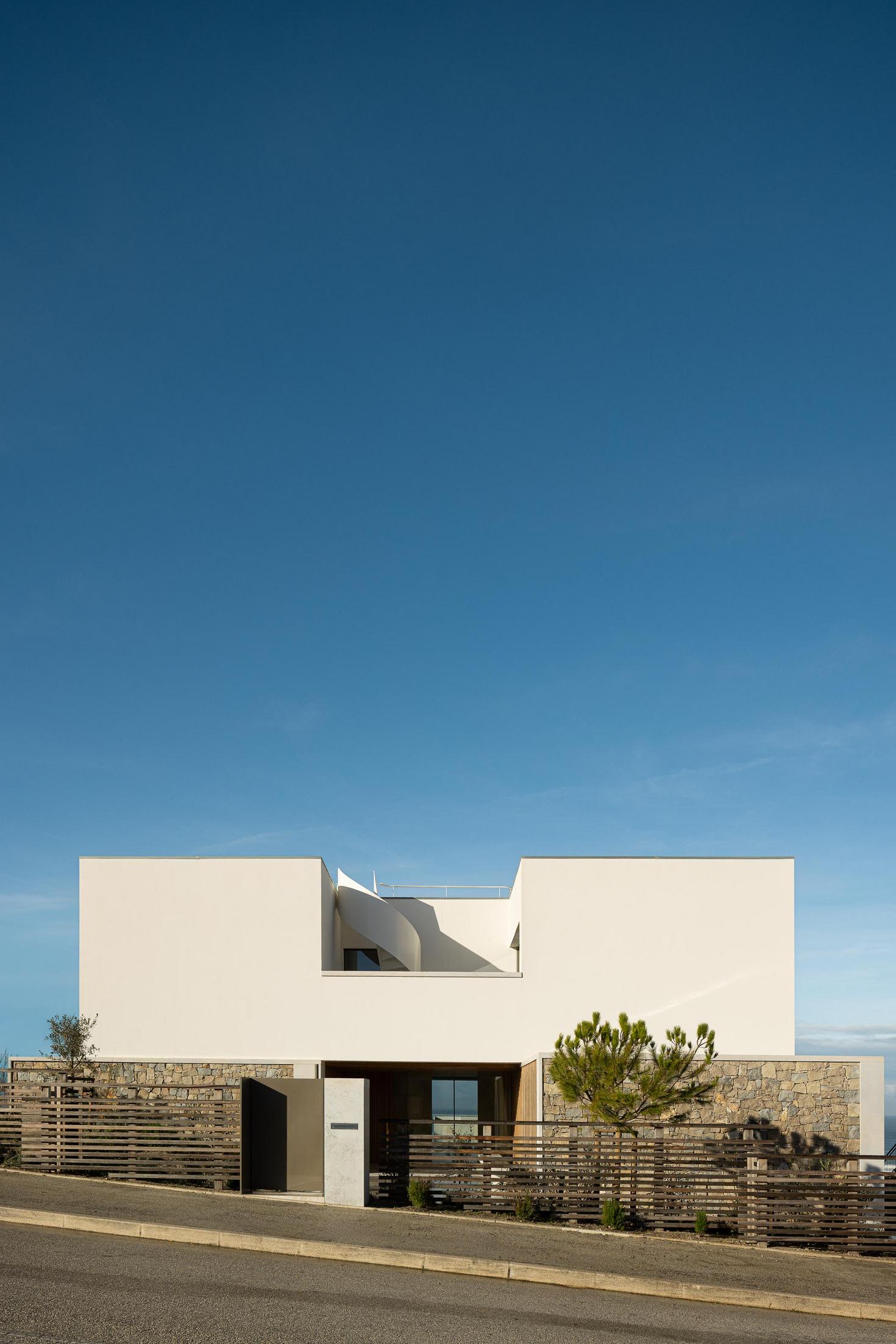 Fachada frontal: Vista frontal da casa com escada em espiral e vedação de madeira horizontal. — WEST CLIFFS D45 arquitetura ARX Portugal - Arquitectos em Óbidos