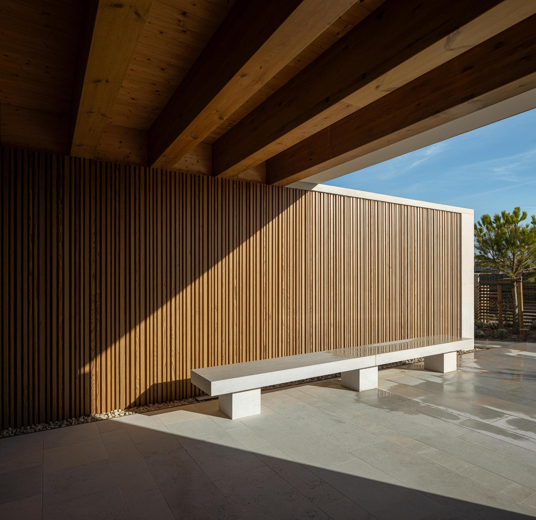 Alpendre: Banco em pedra sob estrutura de madeira com ripas, pavimento em pedra cinzenta. — WEST CLIFFS D45 arquitetura ARX Portugal - Arquitectos em Óbidos